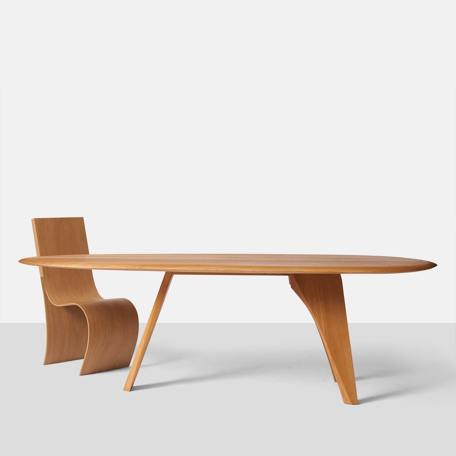 A handcrafted dining table or desk by Belgian artist Kaspar Hamacher. Made in Germany of solid oak from naturally fallen trees. The table features three tapered plank shaped legs and a top that has an oval shape which narrows down on one end. An