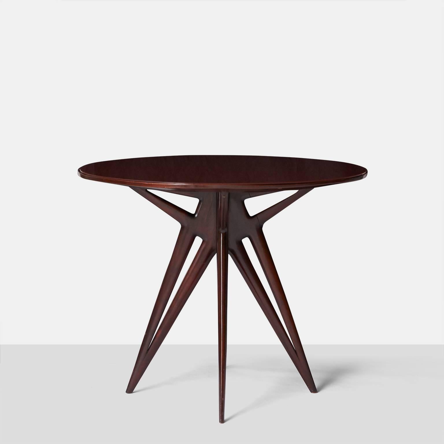 A circular center or side table in rosewood and a deep bordeaux color glass top over three legs with pierced detail.