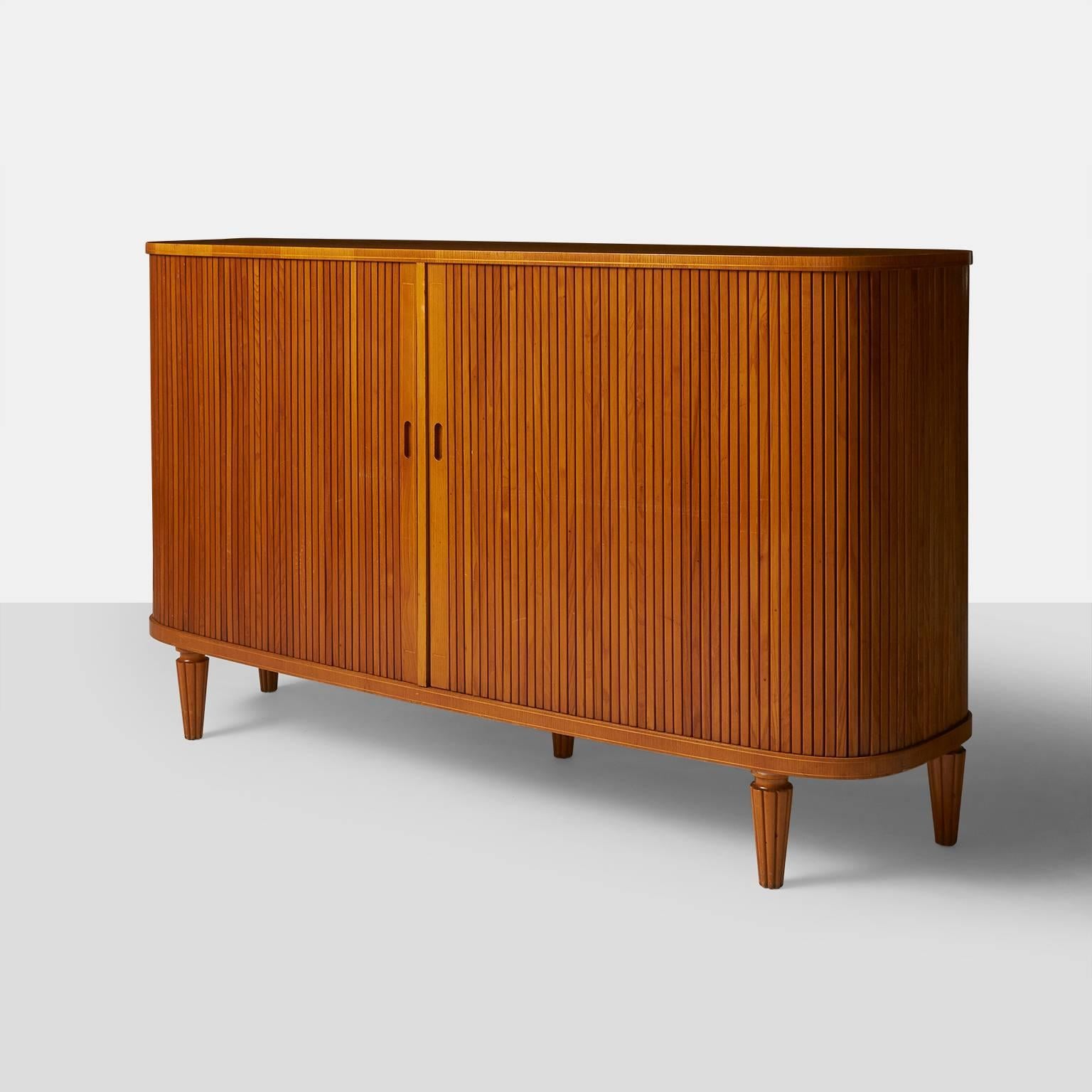 An impressive and elegant Swedish sideboard in elmwood with tambour doors that slide to the back when open. The cabinet is nearly elyptical in shape with adjustable shelves on the interior, three pull-out trays and two pullout drawers. 

   