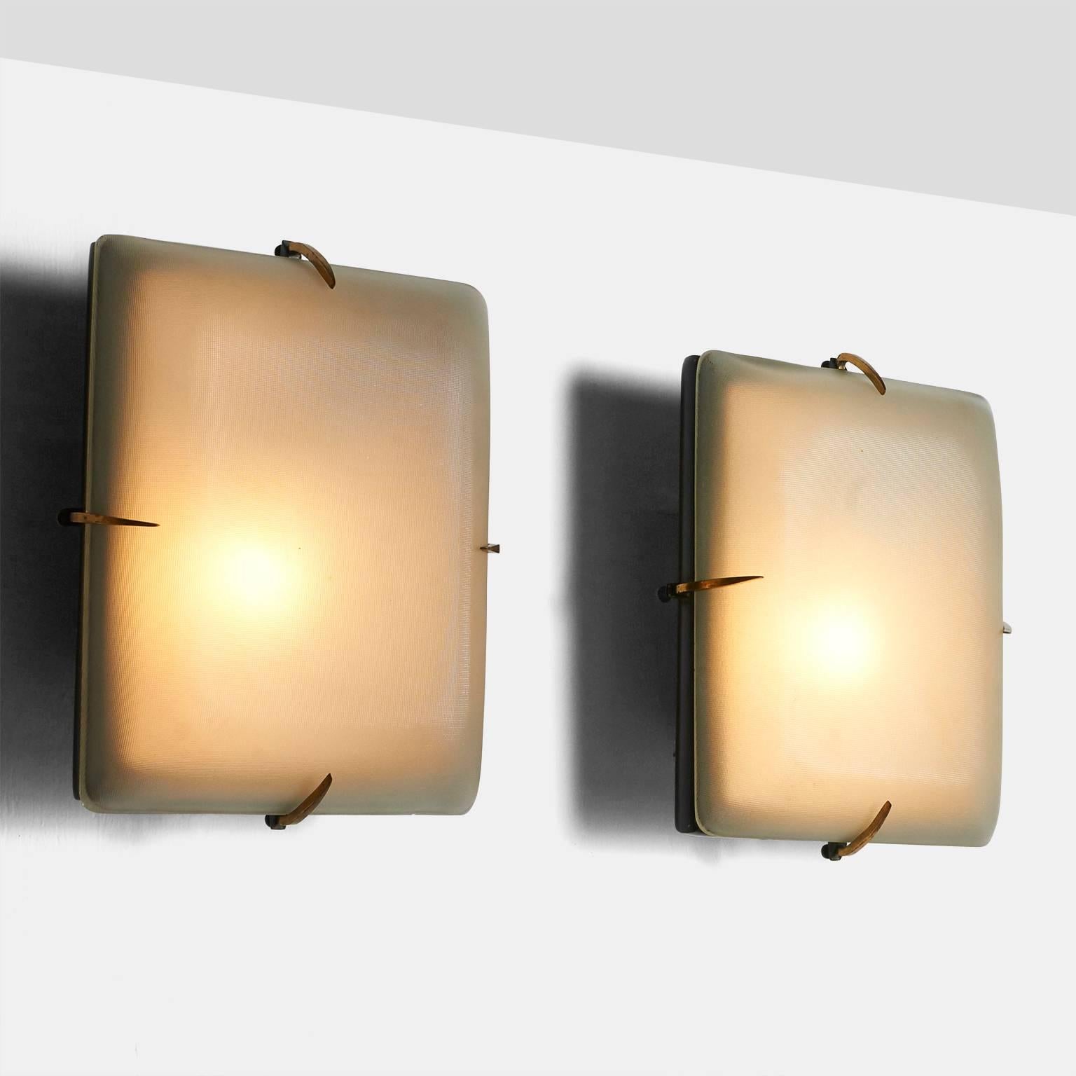 A pair of wall sconces with a black lacquered metal frame with brass trim and brass clamps that attach the textured glass shade to the frame. One Edison base socket. Made in Italy, circa 1950s.
