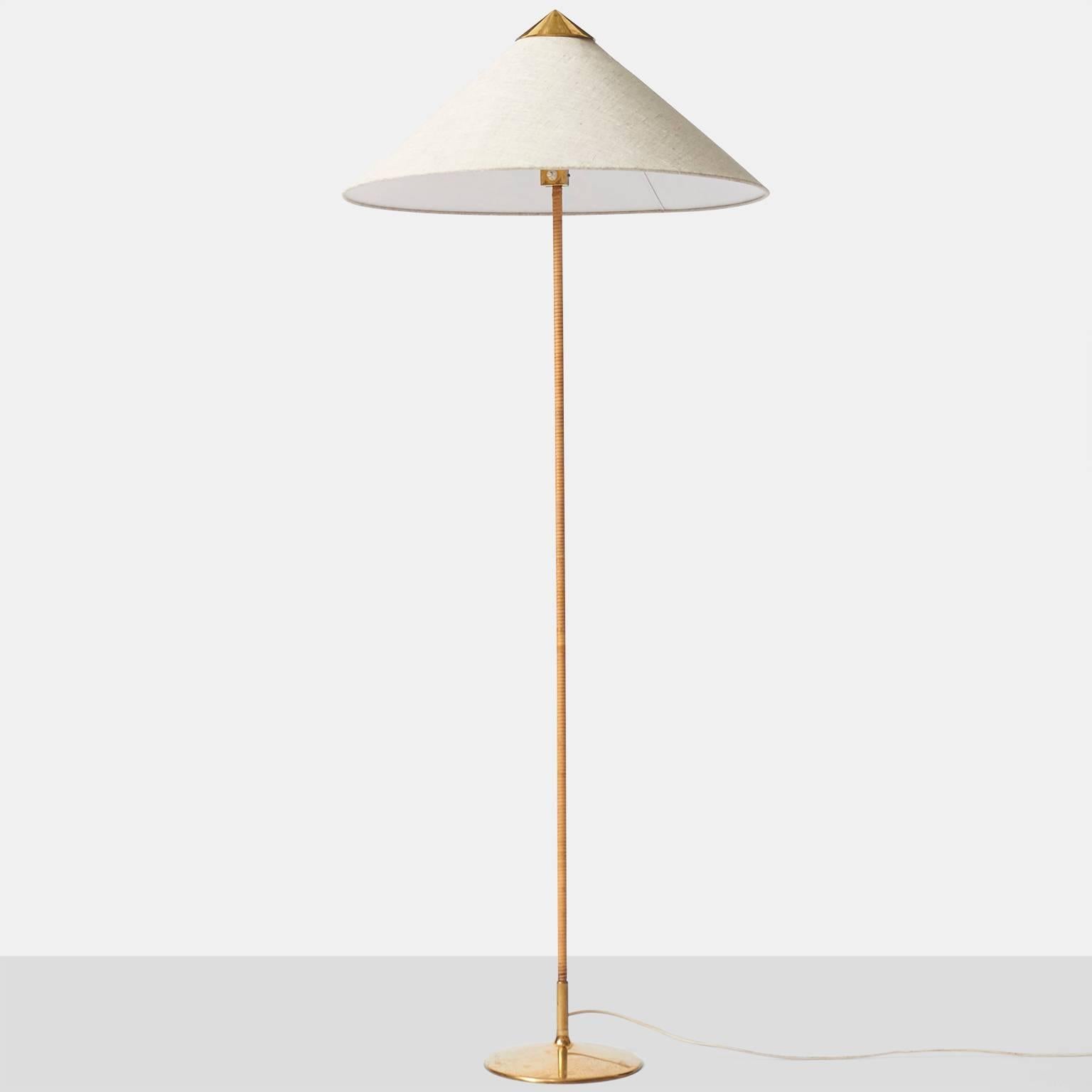 A floor lamp model #9602 by Paavo Tynell for Taito Oy, Finland, circa 1950. The lamp is in brass with the stem wrapped in cane. The 