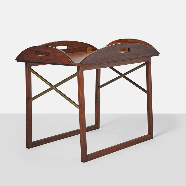 A Butler's tray table, of rosewood on runner legs. Detachable top with flip-down sides. Accents and hinges in brass. Manufactured for Illums Bolighus.