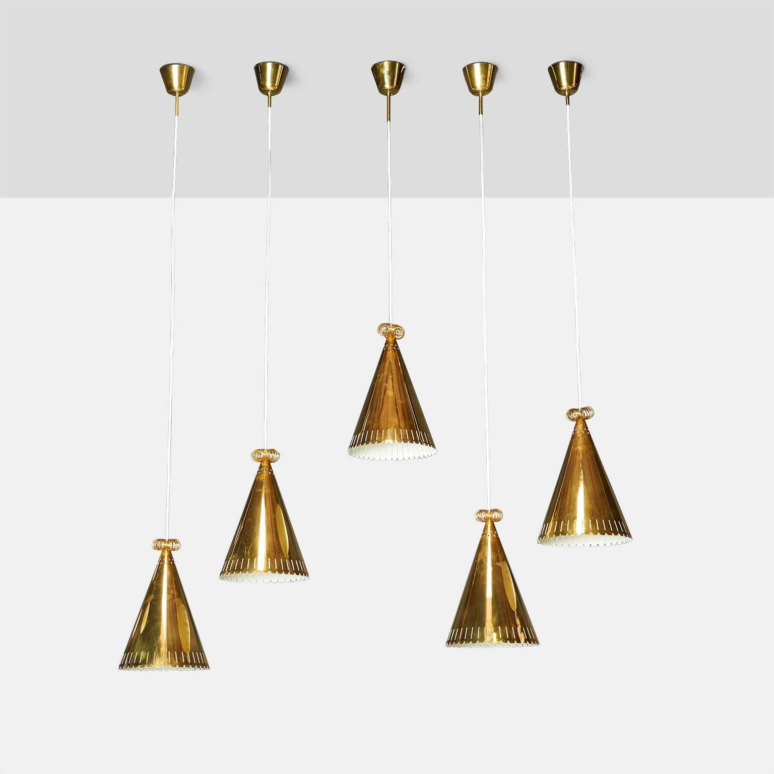 A group of five cone shaped pendants in brass with perforated detail on bottom edge of shade and a brass rosette on top of each. Overall length can be specified. Finland, circa 1950s.