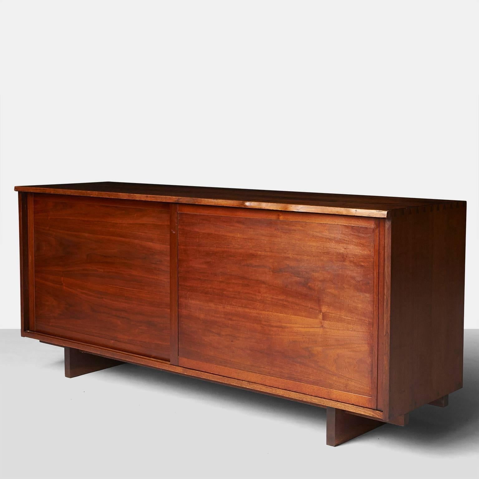 A credenza by George Nakashima in walnut with two bypassing doors and a live front top edge. The interior left side has four pull-out drawers and the right side with two adjustable shelves and one pull-out shelf.
The cabinet is signed with the