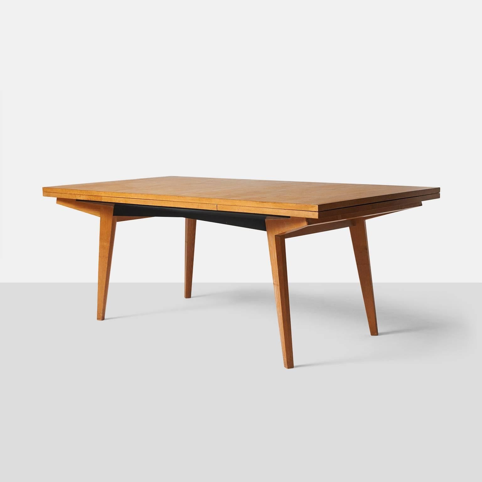 A dining table by Maxime Old in French oak with two leaves underneath that extend on each end to create a 120