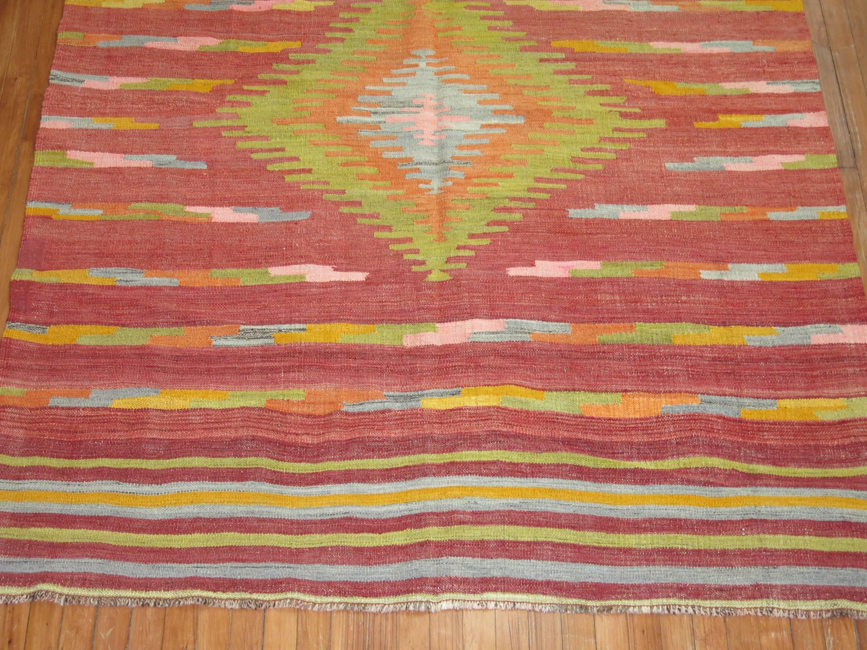 A colorful Turkish Kilim flat-weave rug. Large-scale lime green medallion with accents in orange, pink, gray on a burnt red field with a striped motif on both ends.