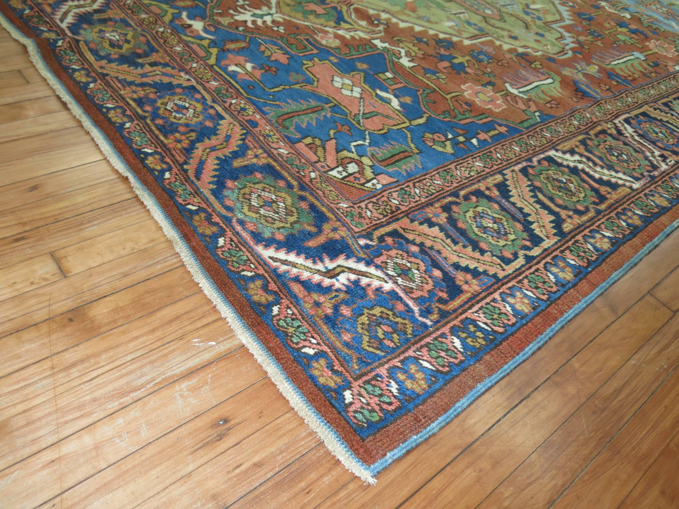 An antique Persian Heriz Carpet featuring a green medallion, orange field, blue border and predominant accents in rusts, terracotta and french blue.
