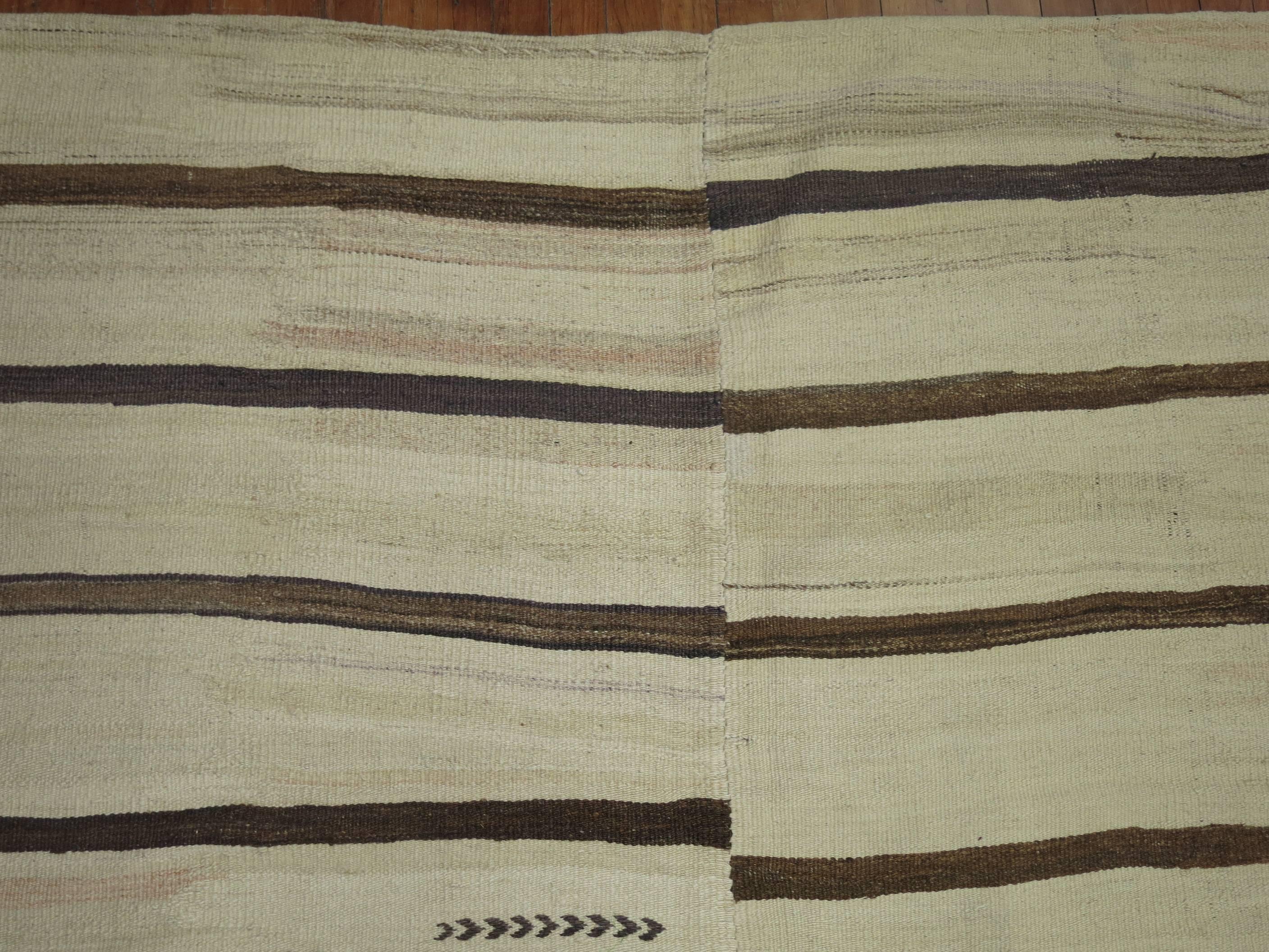 An interesting oversized one of a kind striped Turkish Kilim predominantly ivory and brown with a few nomadic elements. Two pieces woven together intentionally for the purpose of covering a large space.

12'1'' x 14'1''