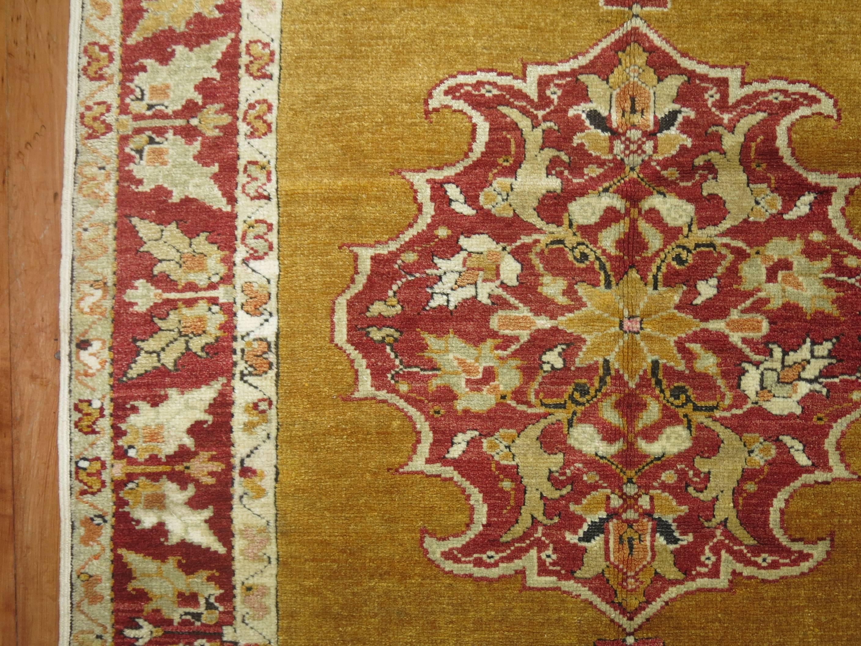 Exquis tapis turc Melas avec un fond de couleur moutarde, une bordure rouge profond et un médaillon central.