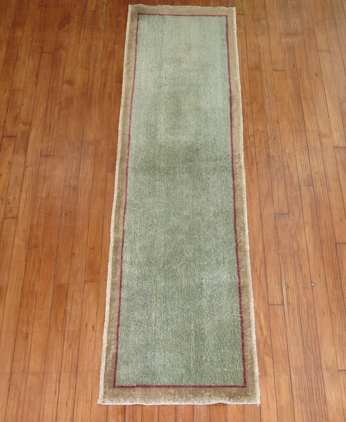 Vintage Turkish runner with a solid green field outlined in red encased by a brown border.