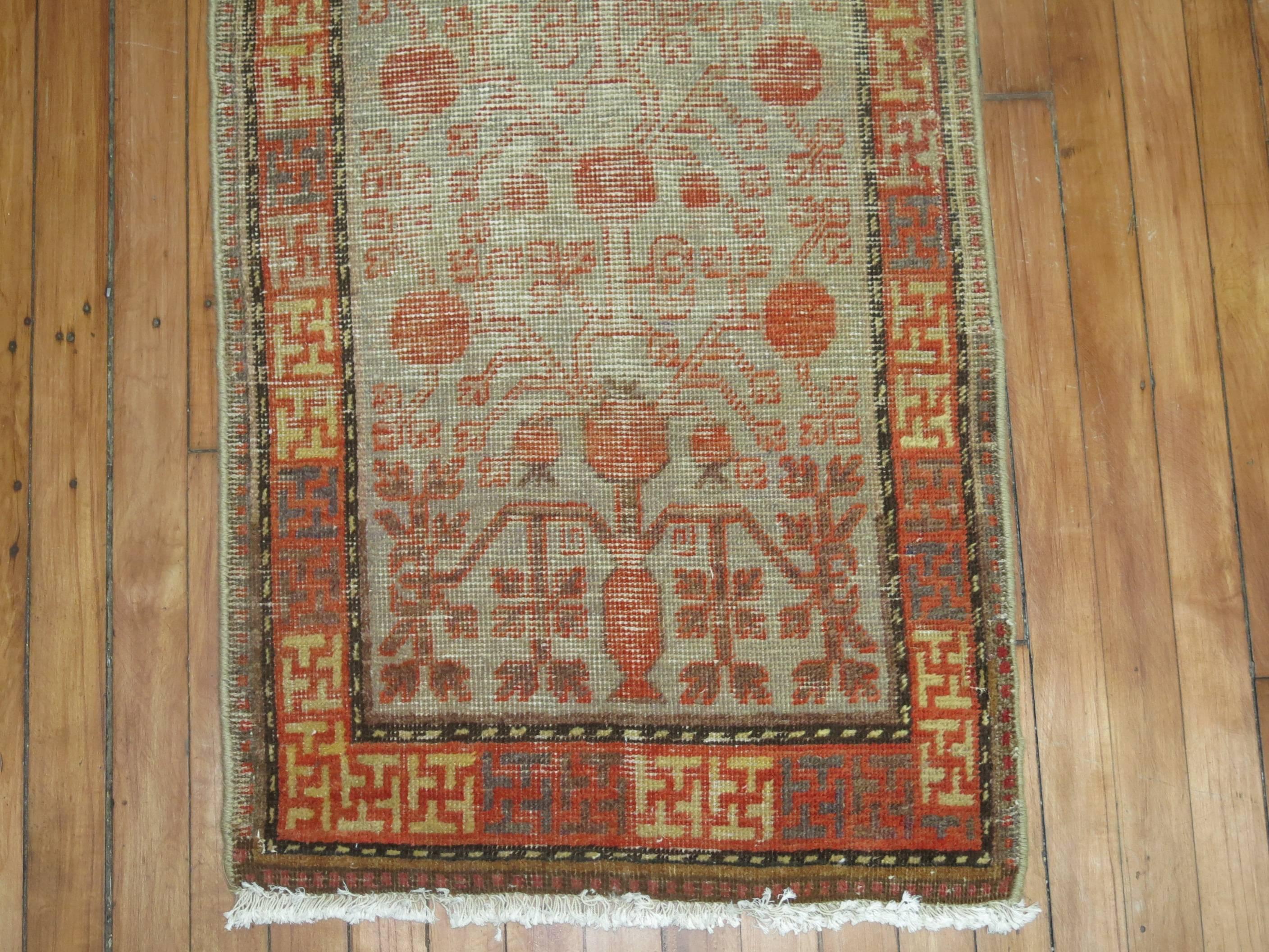 Small worn Khotan runner with a pomegranate design surrounded by a intricate border.