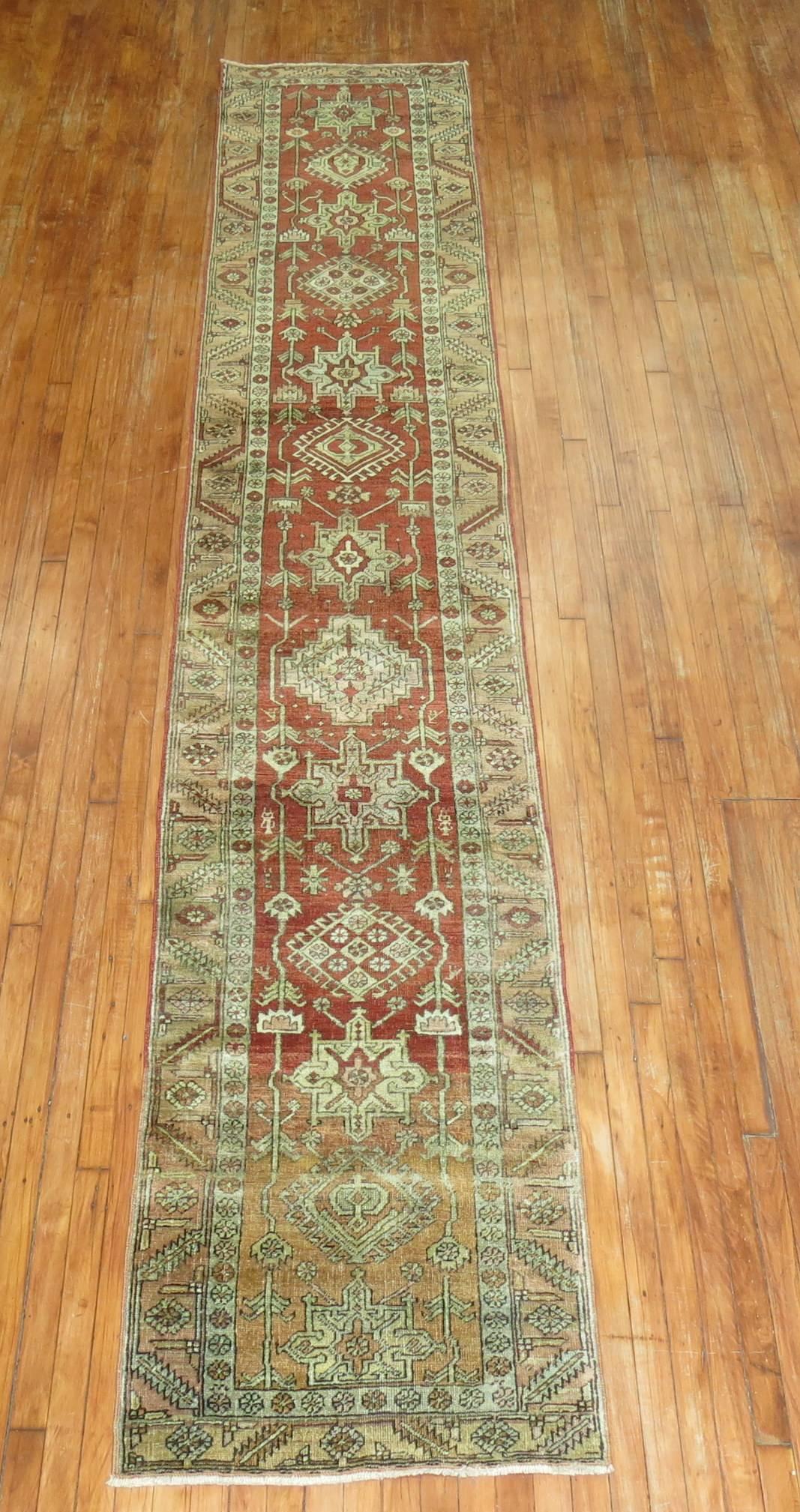 Narrow and long vintage Persian Heriz one of a kind runner with a brick red field with 1 end having an abrash variation in a burnt orange color. Abrash is a term used to describe color variations found in hand knotted Oriental rugs. Although such