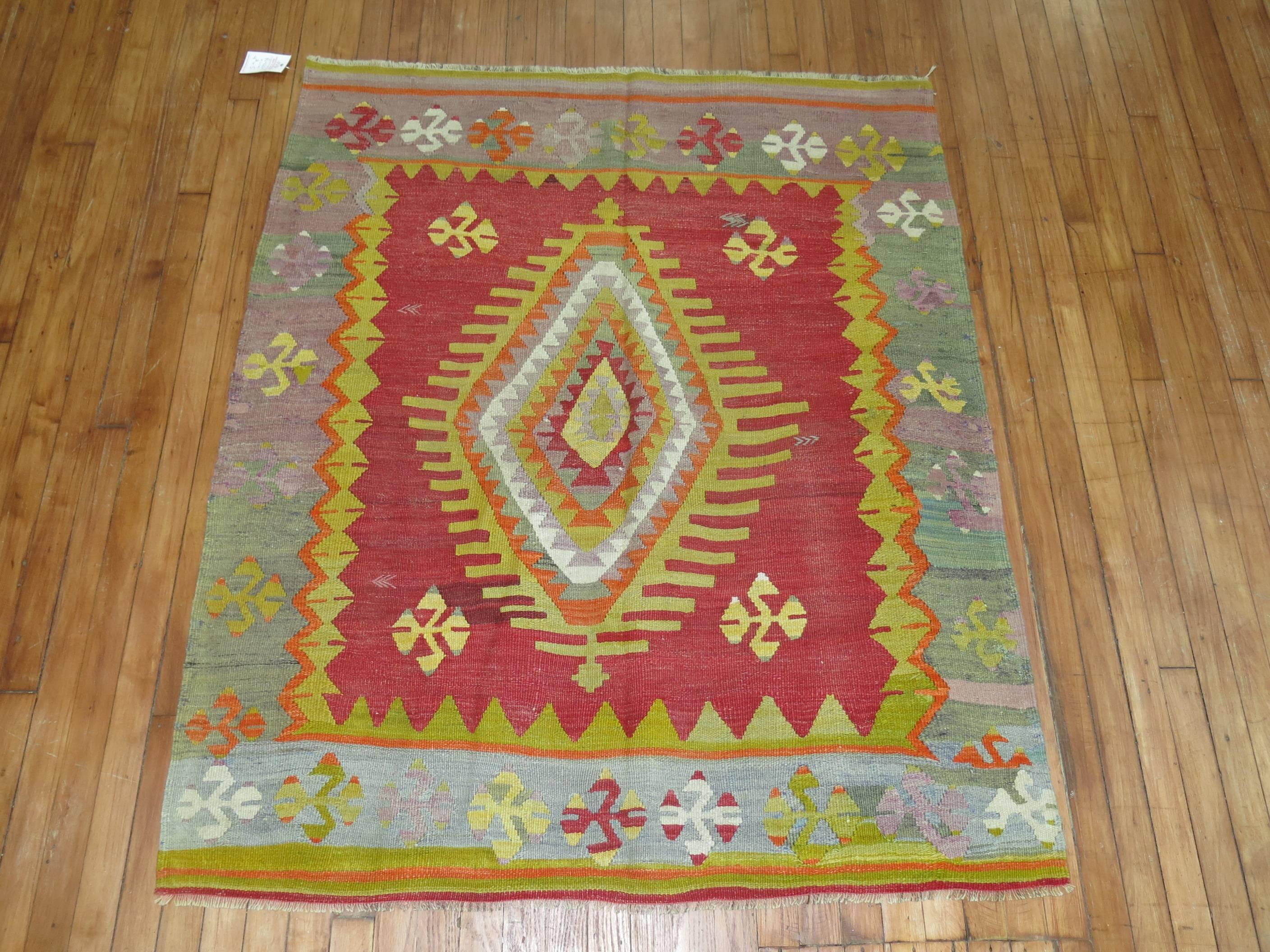 A one of a kind vintage Turkish Kilim with a traditional central medallion and border design. The field is a bright red, accents in dominant lavender and green accents

Measures: 4'2” x 5'.