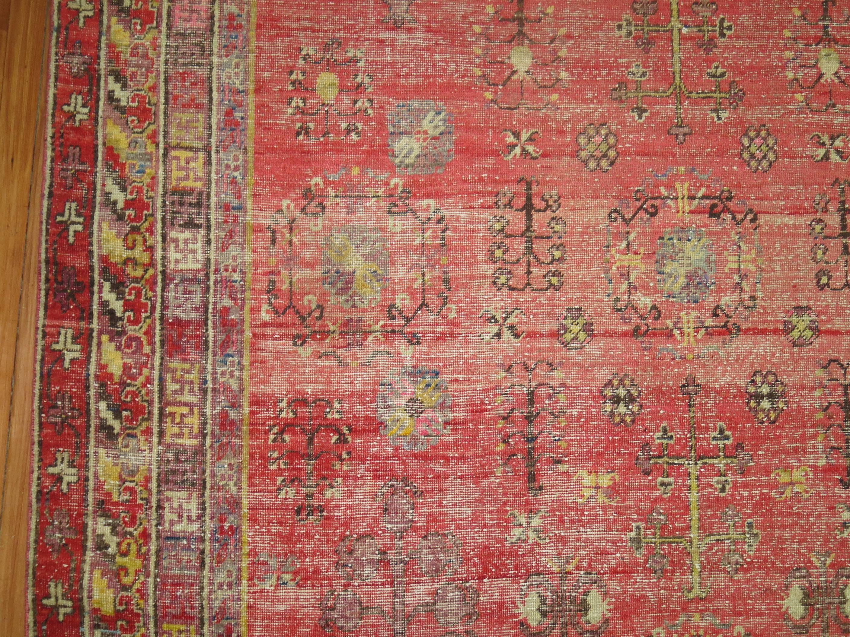 A shabby chic antique khotan rug in predominant pinkish/red