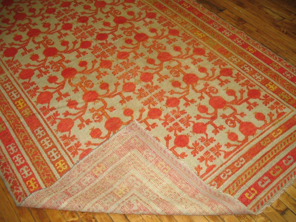 A fun and cheerful Khotan rug containing a pomegranate pattern that lies on a celadon background with lime green, watermelon and yellow color accents.
