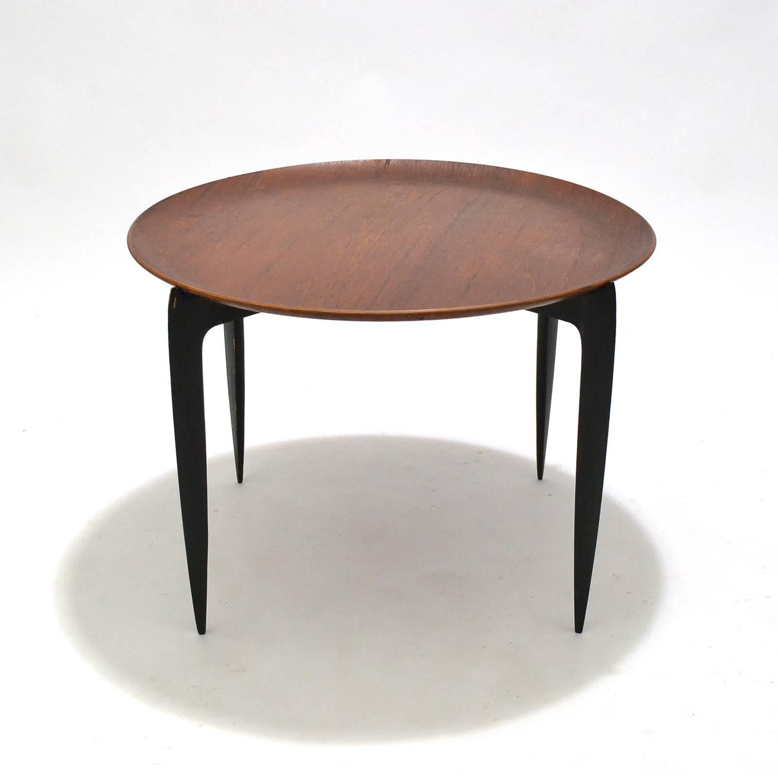 Light, leggy, and incredibly useful, this tray-top table designed by Svend Aage Willumsen & H. Engholm and made by Fritz Hansen folds flat for easy storage when not in use. When open, the sleek tapered black legs support the teak top with a raised
