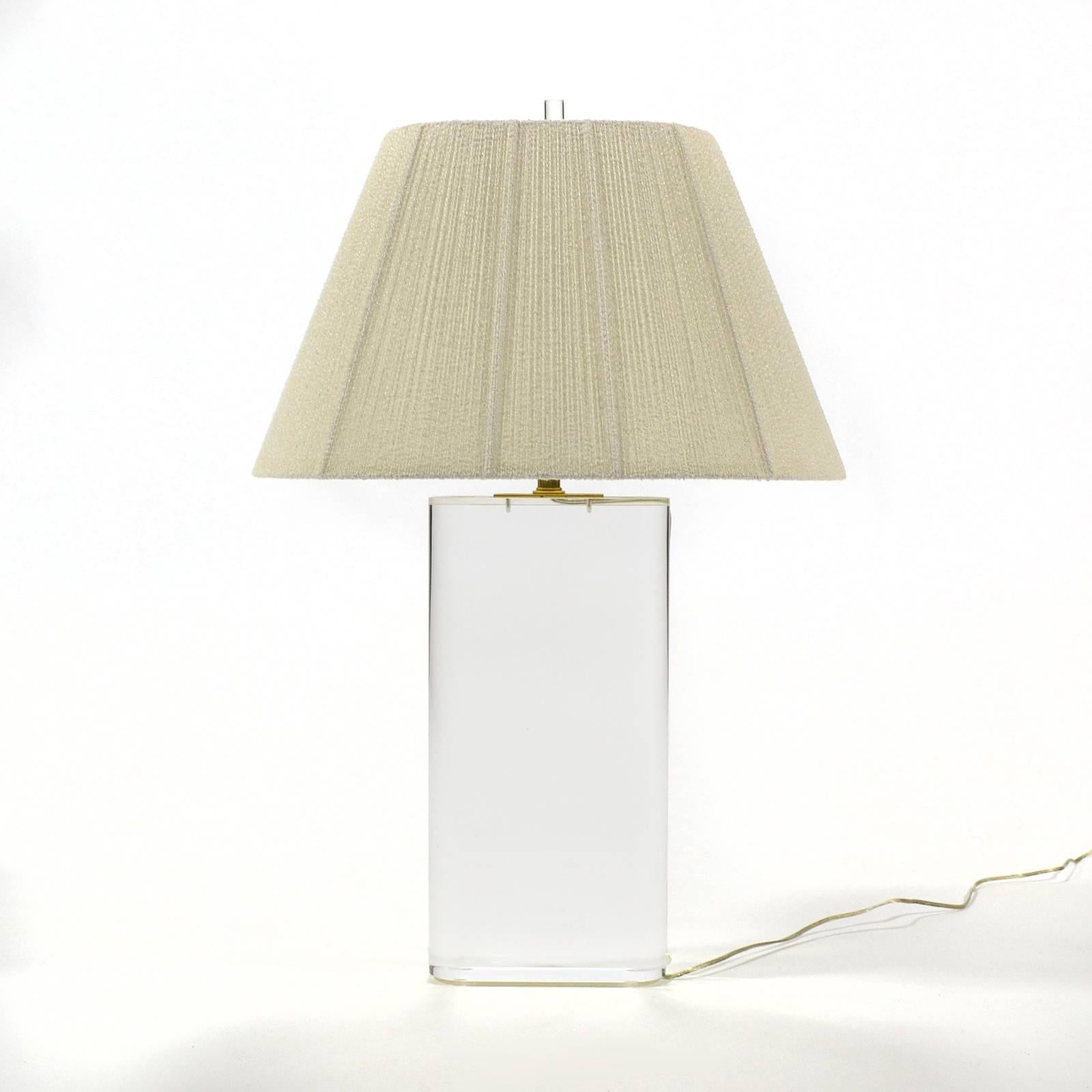 This spectacular table lamp has an oval base of three inch thick Lucite, the finest quality brass hardware, a perfectly matched shade of silky string and matching Lucite finial. The spare minimal form perfectly compliments the transparent material