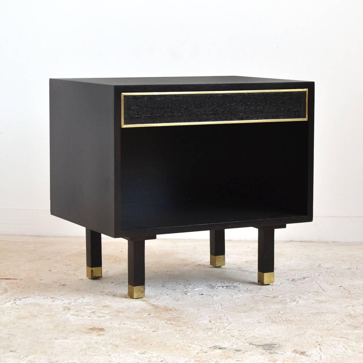 A lovely little end table or nightstand in mahogany with a rich, dark finish and brass details. It features a single shallow drawer over an open cabinet.
