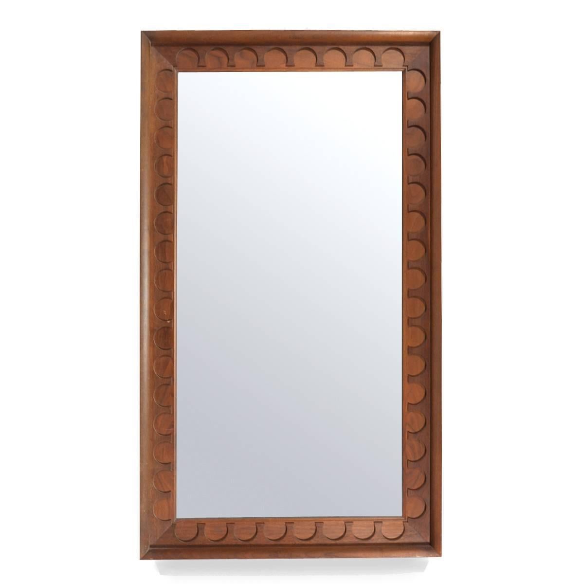 This substantial mirror has a frame of walnut with a terrific carved pattern. Designed by Arthur Umanoff while working in the George Nelson office, these were offered in other sizes and shapes by Howard Miller. Measuring 50