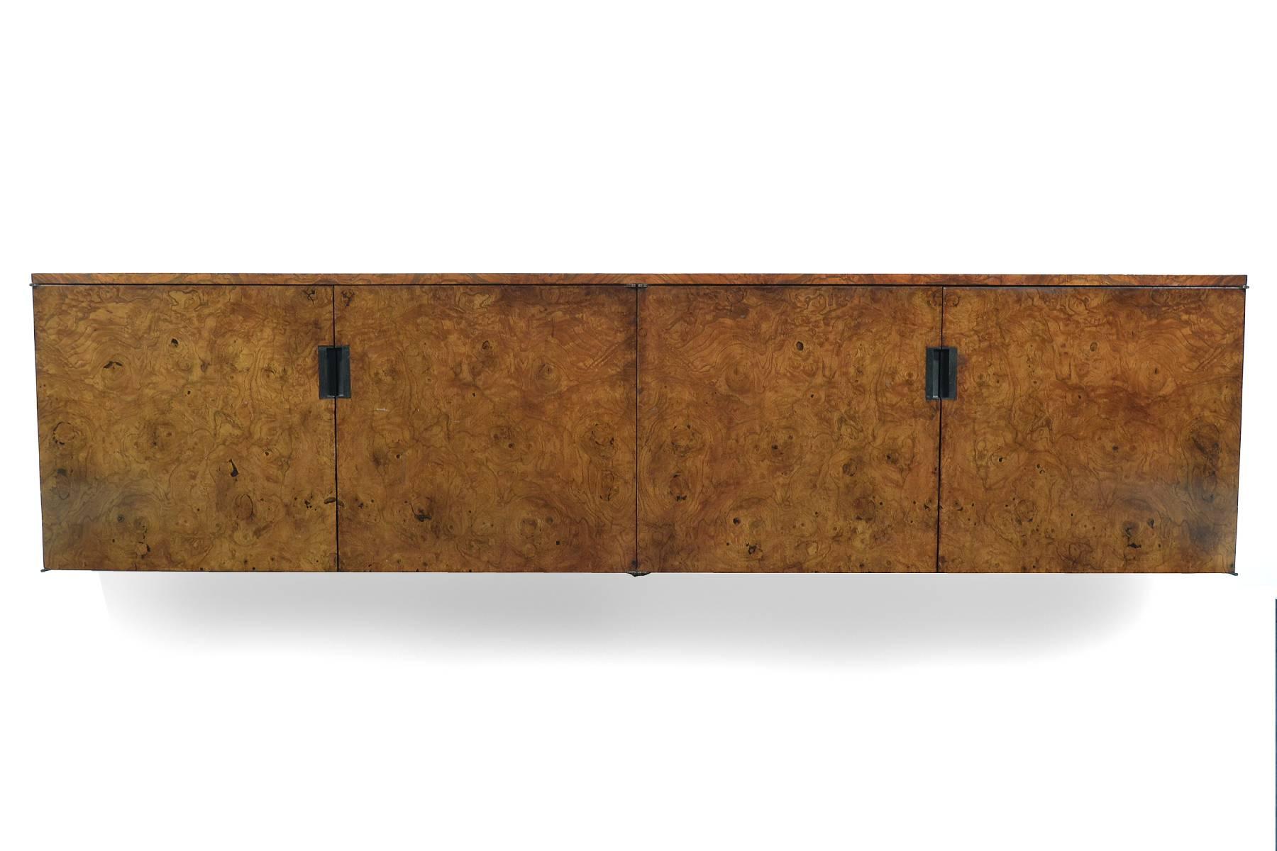This handsome Sprunger wall-mounted credenza combines a Minimalist form and richly variegated burled olivewood. The cabinet features two doors concealing two adjustable shelves and two shallow drawers. The pulls are a very attractive inset design