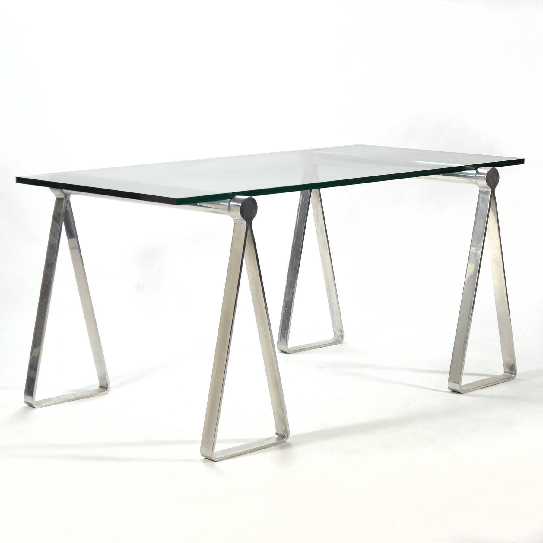 An ingenious and attractive design. Two Campaign-style aluminum sawhorse forms support a glass top creating a wonderful desk or table. The original glass shows damage– ordering a new glass top saves on shipping cost and allows you to select the