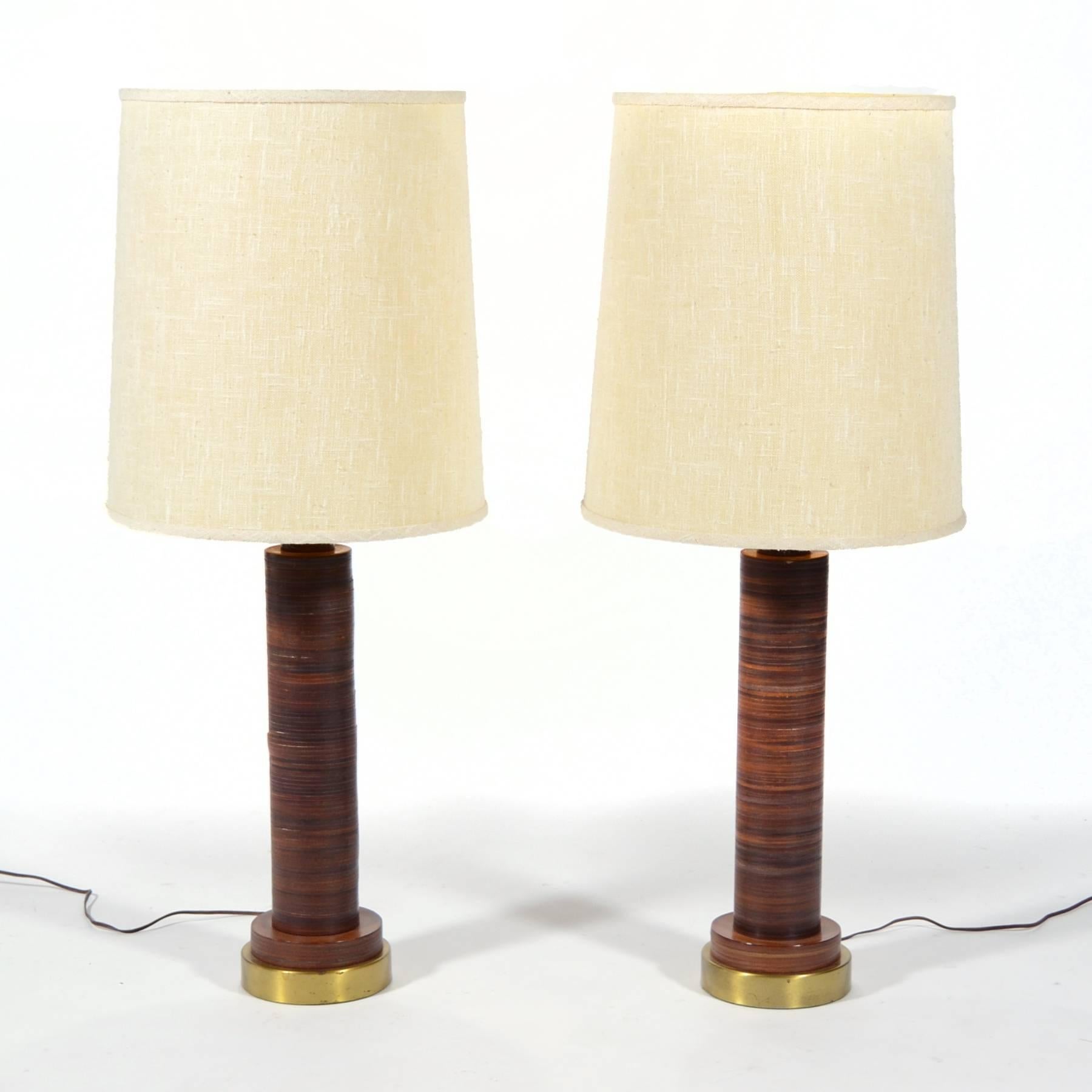 This handsome pair of table lamps have bases made of stacked leather. The leather imparts a richness and the striations add visual interest. The lamps have brass bases, brass hardware, and are topped with what appear to be the original ivory linen