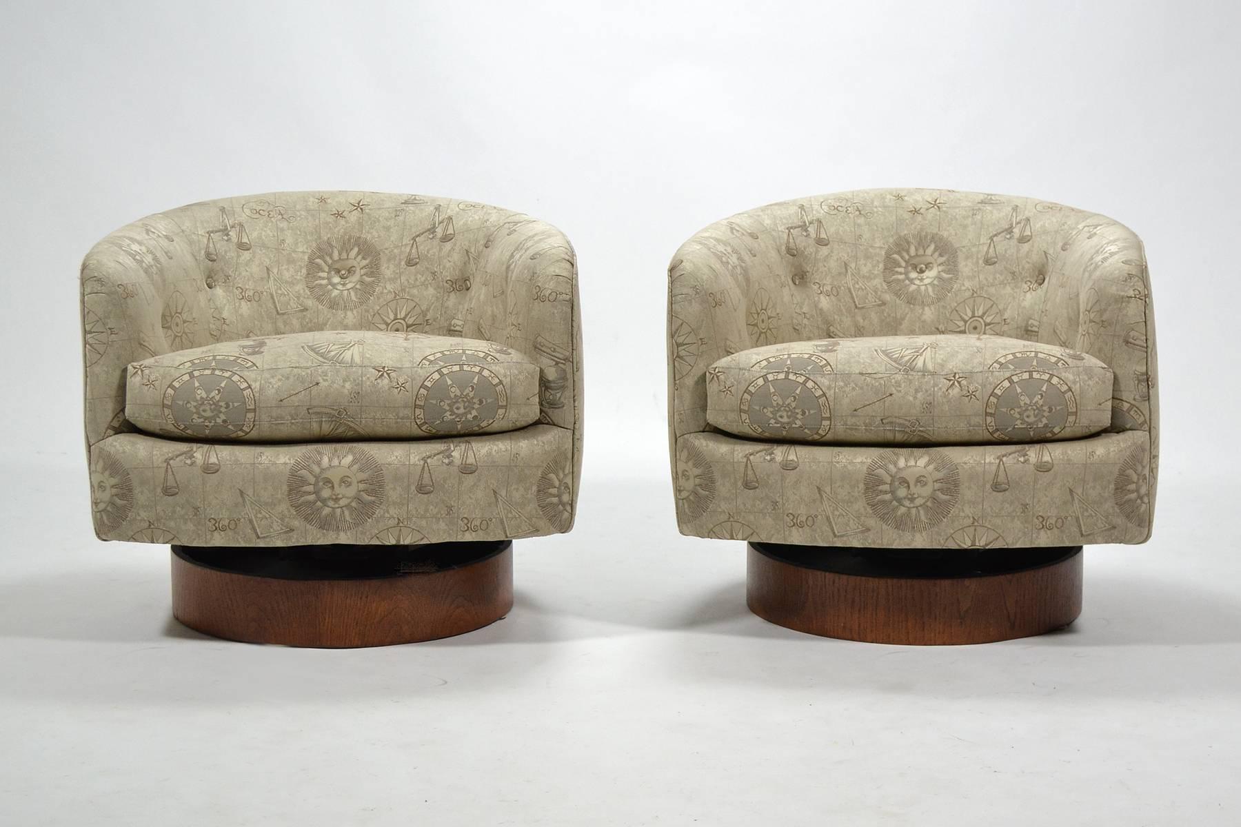 This pair of Baughman lounge chairs are very comfortable with their swivel and tilt function. The barrel back forms sit atop cylindrical walnut bases. They are upholstered in a zodiac-themed fabric which reminds us of Fornasetti.