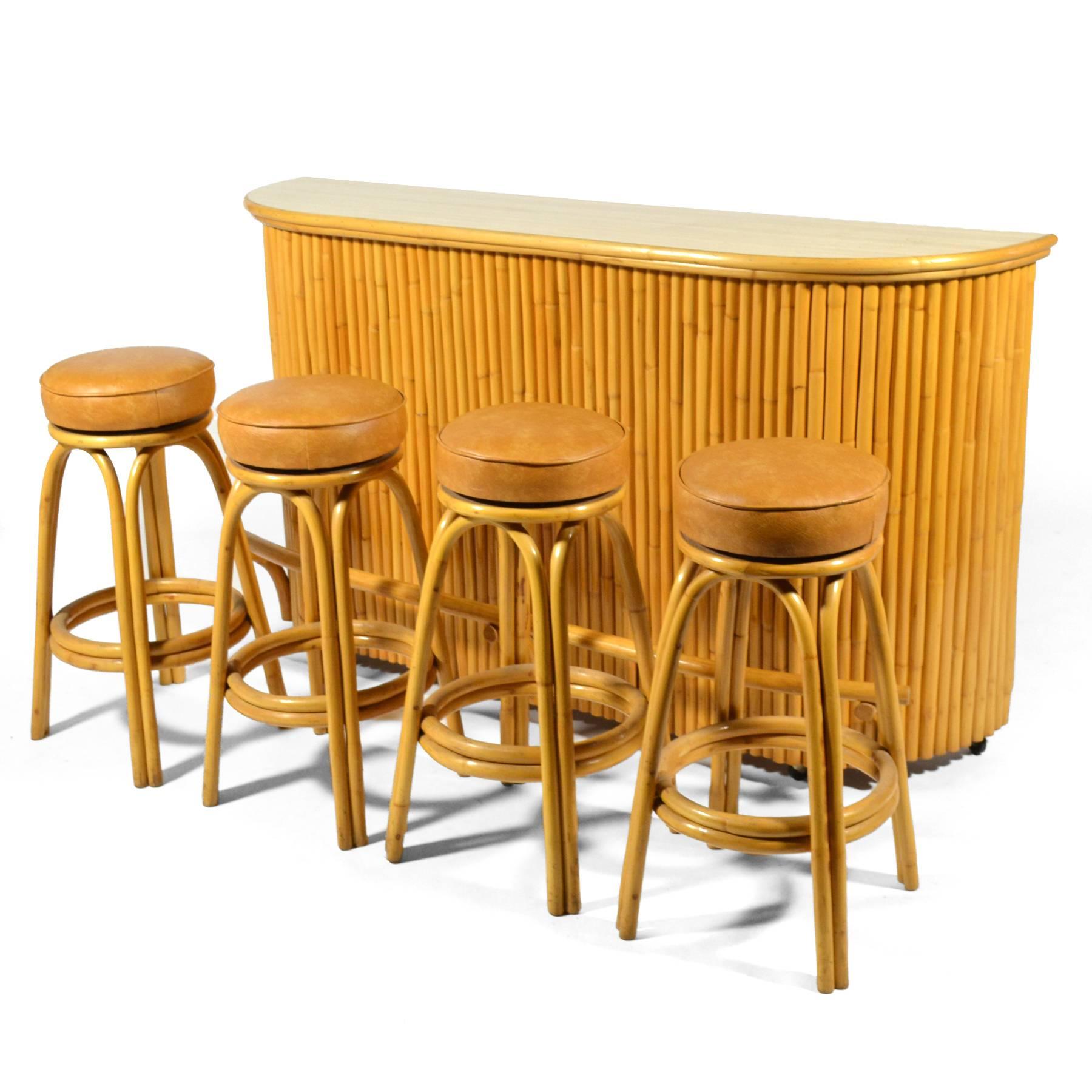 This wonderful rattan bar and matching stools exudes tropical Tiki chic. A beautiful vintage example in great condition, it has a great scale, a curved front, a footrest, two shelves a cutting board and a drawer in the back. The stools have