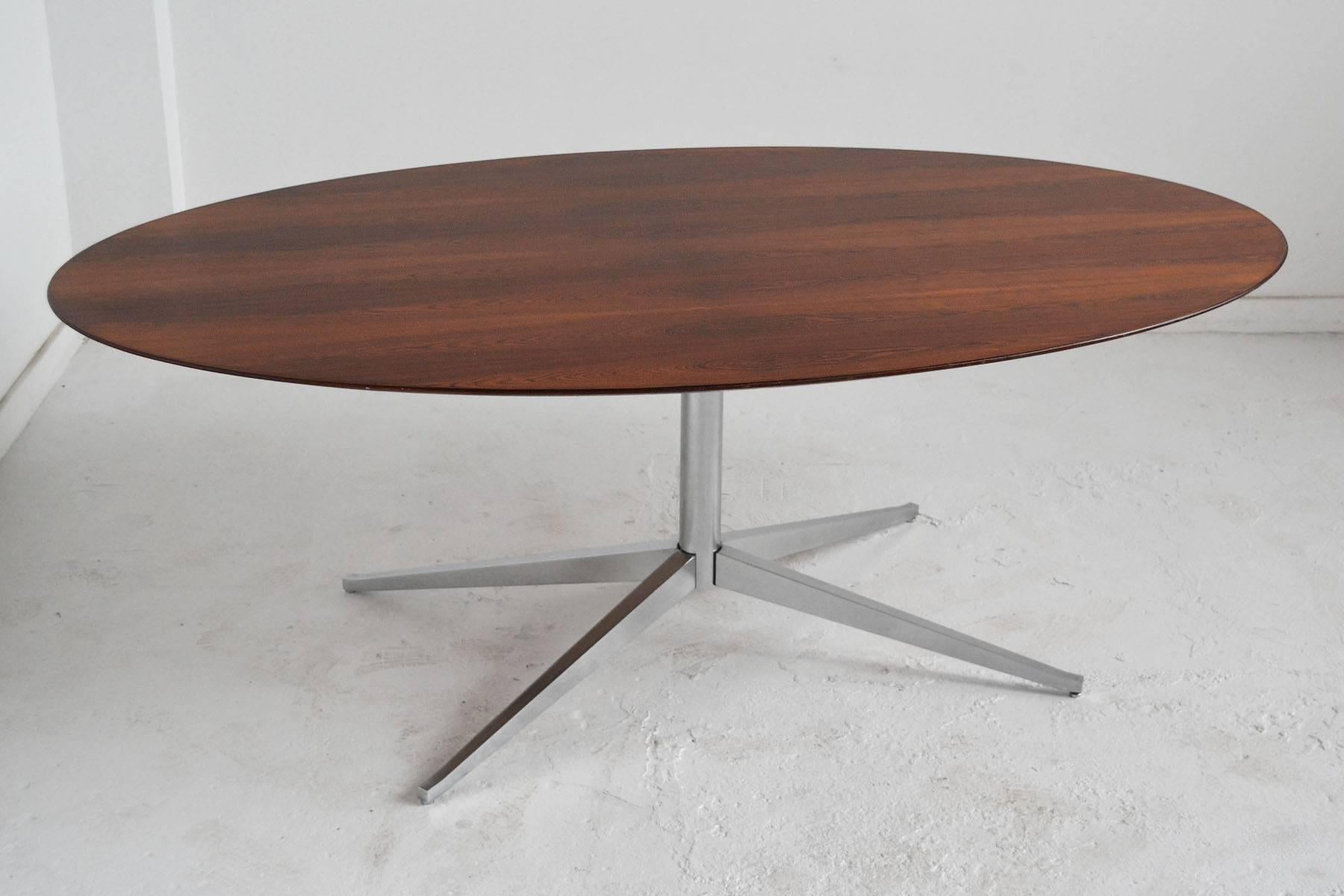 The beauty of the elegant form is equalled by the rich rosewood top of this table by Florence Knoll. It can serve as a dining table, conference table, or desk. Supported by an X-shaped pedestal base, the top is elliptical in shape and the underside
