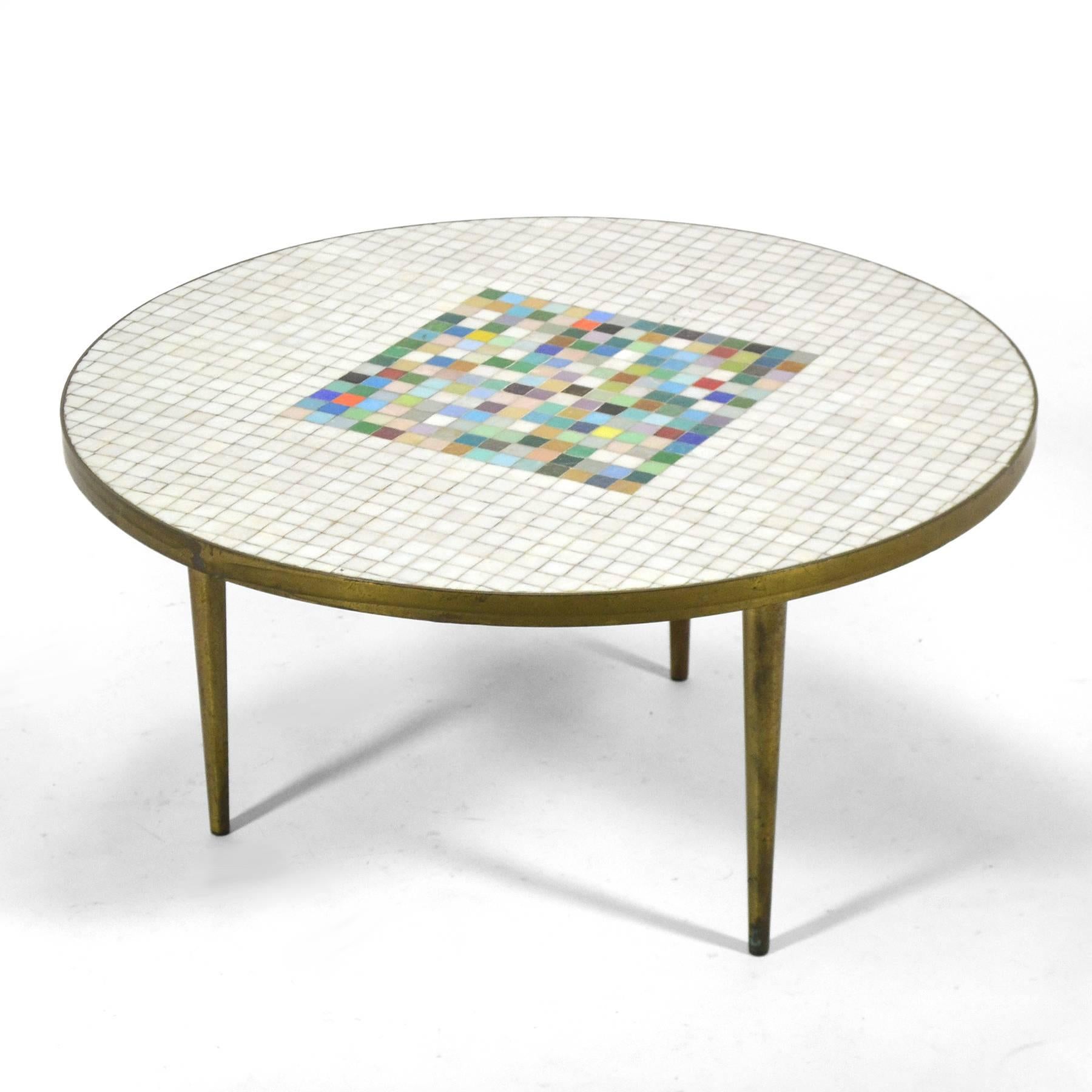 A striking table with a top of Murano glass tiles set in a brass frame supported by three tapered brass legs.