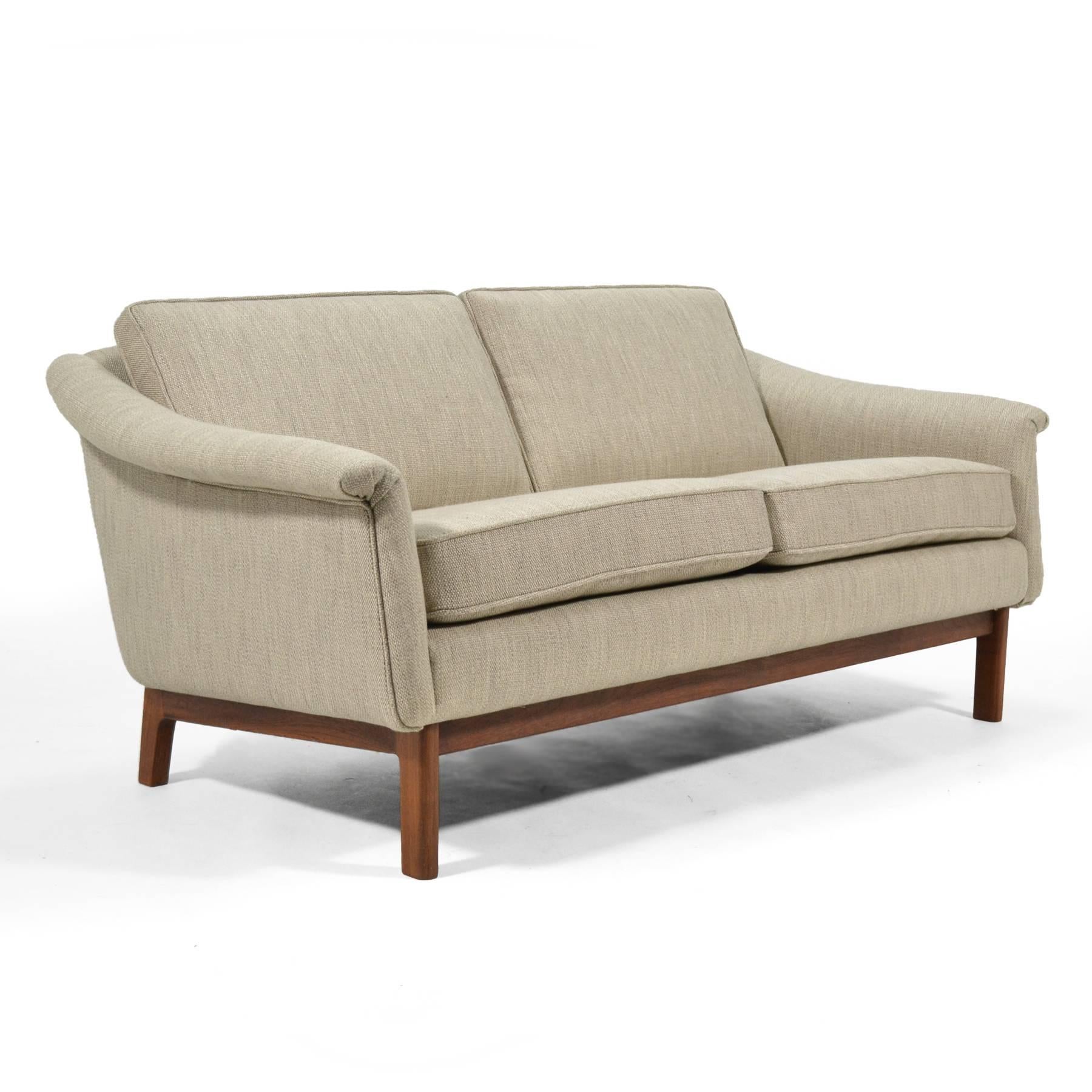 This two-seat by Folke Ohlsson has a terrific scale and an upholstered body with soft contours supported by a walnut base. Newly upholstered in a textured warm grey fabric, it is well suited for any interior.
