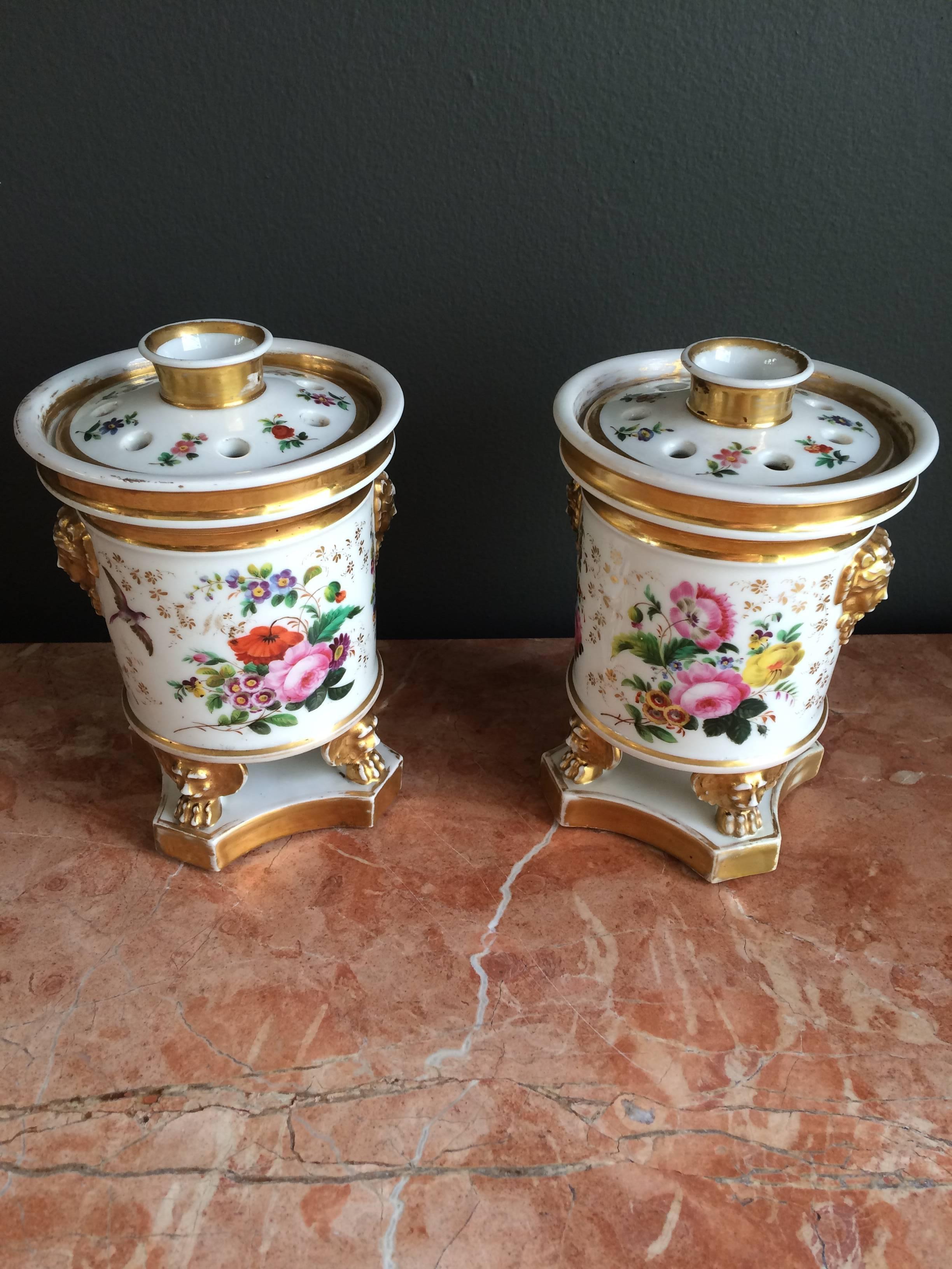 A charming pair of footedbcircular floral design potpourris with gold trim and decorative mounted masks on either side with removable lids.