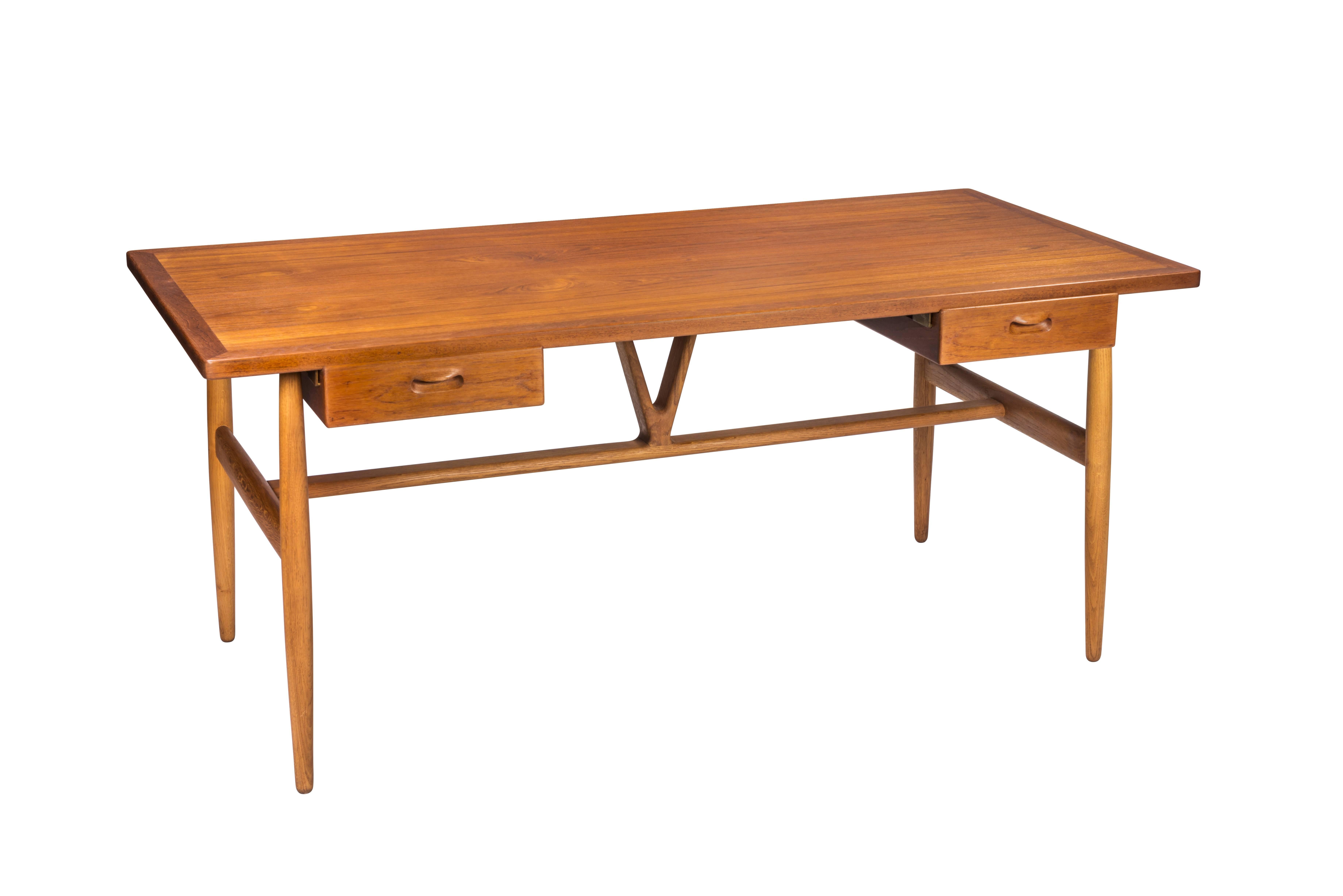 A rare and nicely designed and detailed writing desk having a teak top over two floating drawers on turned oak dowel legs braced by a hand-carved central wishbone-shaped strut. Iconic Danish design. Signed.