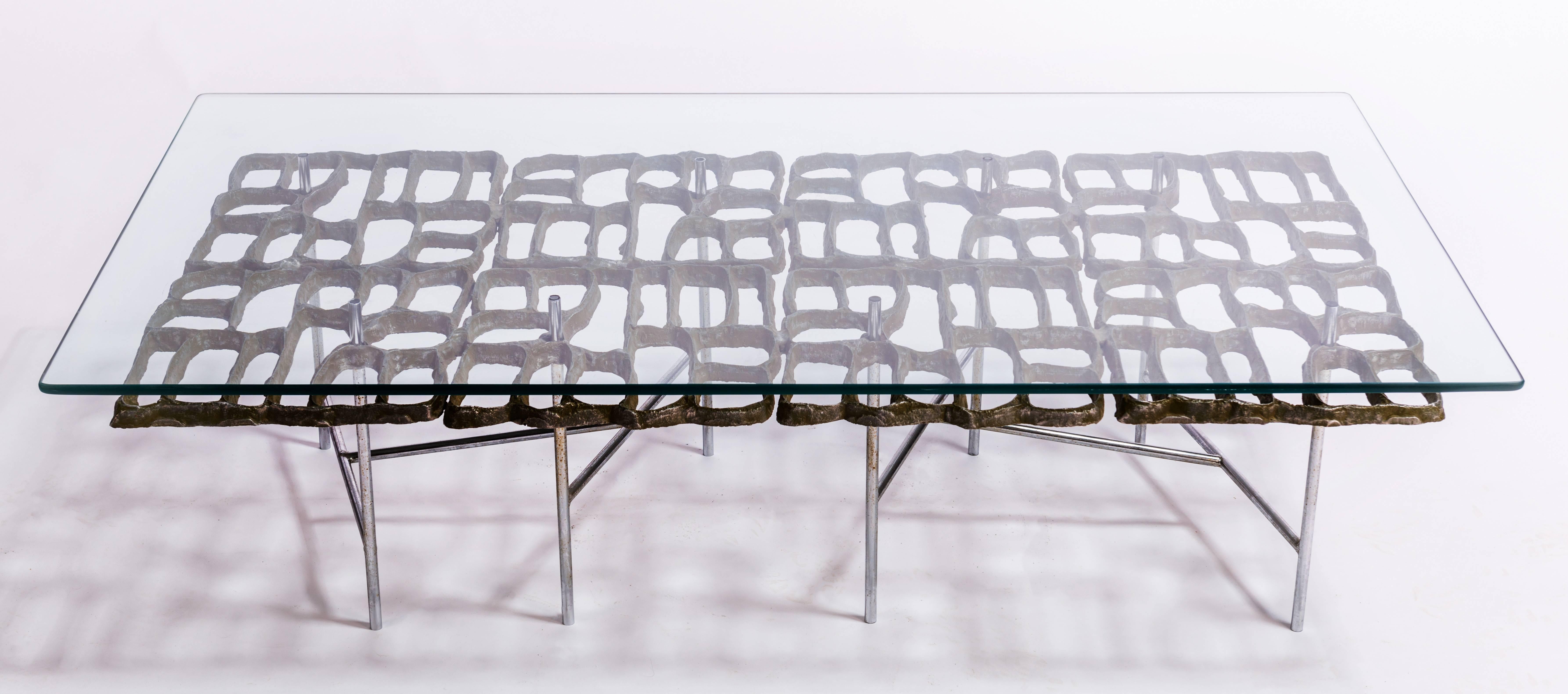 Interesting Brutalist coffee table by noted American sculptor and designer Donald Drumm. Coffee table with a tubular metal frame that supports a cast aluminum design and a rectangular glass top.