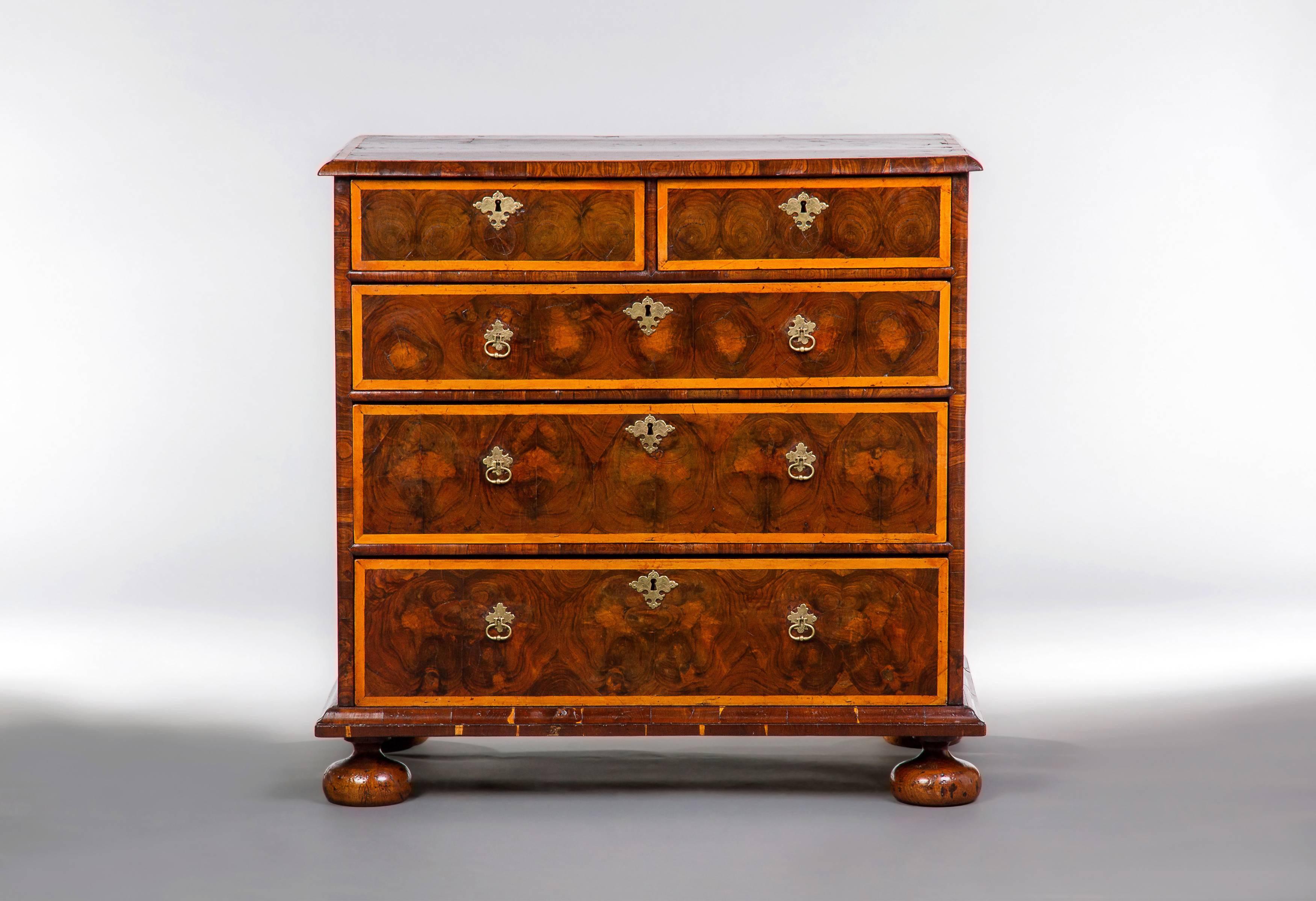 The oyster veneers in olive wood with line inlay and banding in Hollywood, the lower molding in cocus wood, with two short and three long drawers all raised on turned bun feet. The decoration to this chest is in superb condition and the arrangement