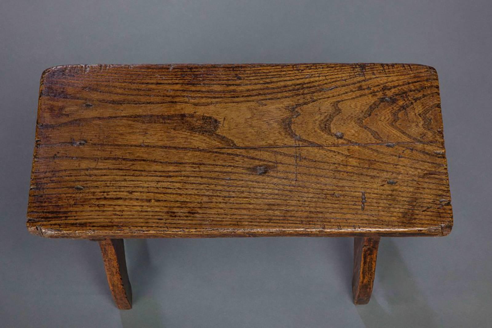 Of boarded elm with a plank seat and ogee cut end bounds united by a turned stretcher. This rustic stool was made in the style of the late 16th century.

English, circa 1800.