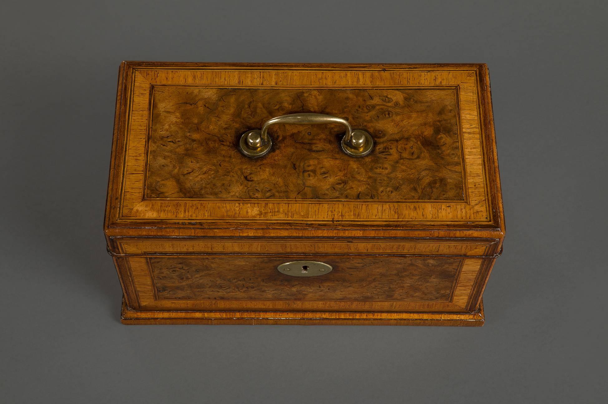 In very well figures burr walnut and cross banded with padouk. The hinged rectangular top with a brass handle opening to a fitted glass mixing bowl flanked by compartments for tea canisters, on a molded plinth.

English, circa 1730.