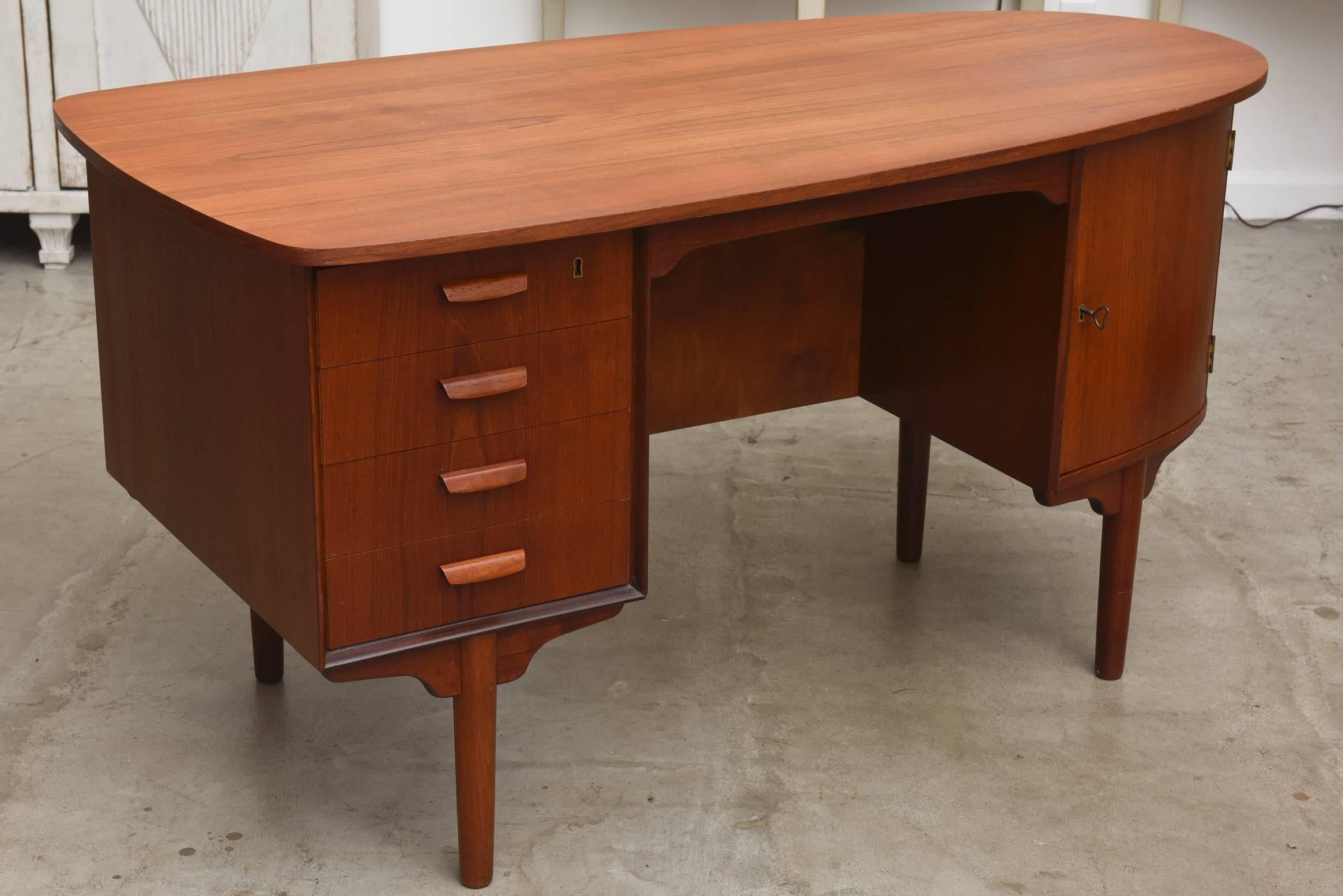 Vintage 1950s Danish Mid-Century Modern teak desk, in an unusual asymmetric streamlined shape with a curved side. The front has four drawers and a cabinet with pullout trays and shelves. The back features a cabinet and two shelves. Original hardware.