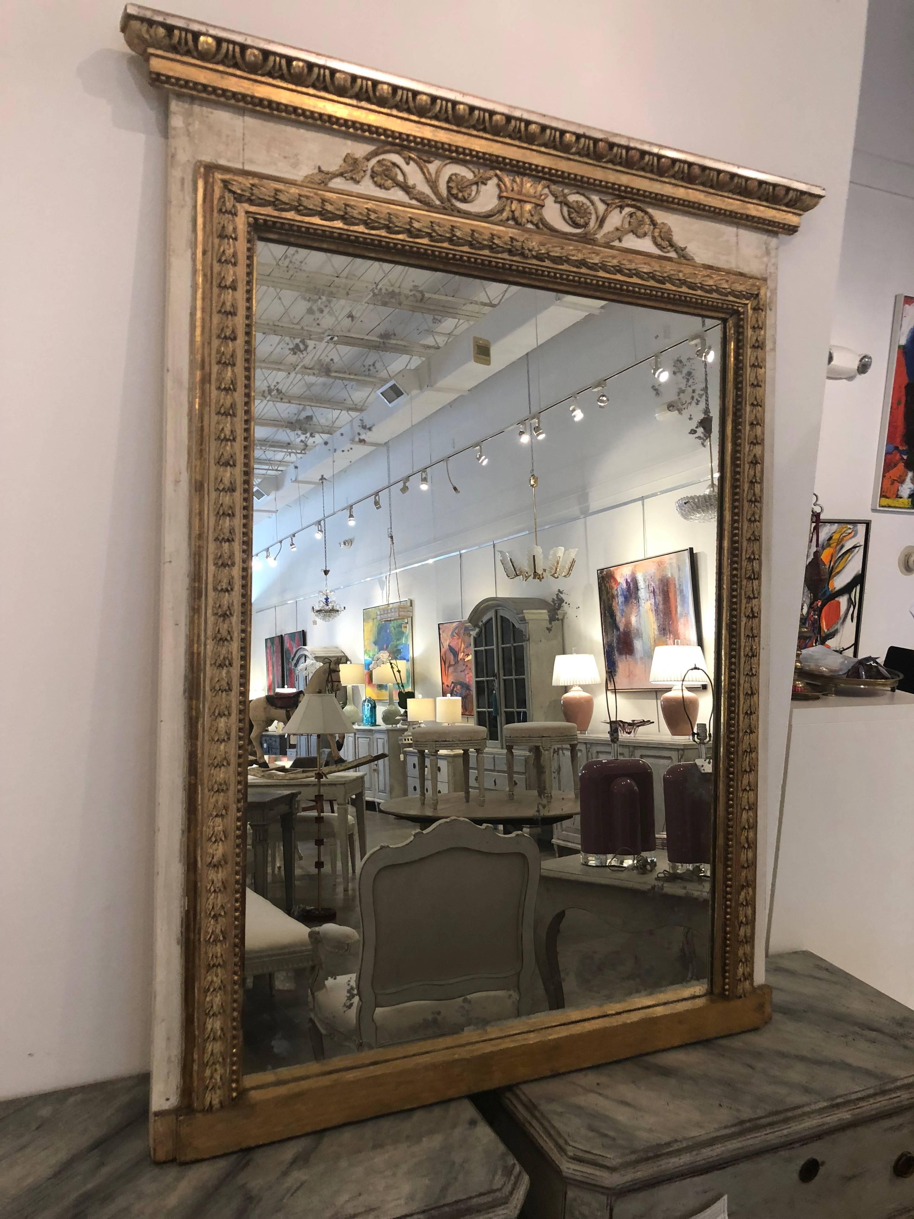  Antique Swedish Gustavian Trumeau mirror,  with distressed Swedish white paint and gilt framing.
The mirror is surrounded by gilt wood connected leaves and above the gold frame
 is lovely carvings of pinecones and pearl beading, topped with an egg