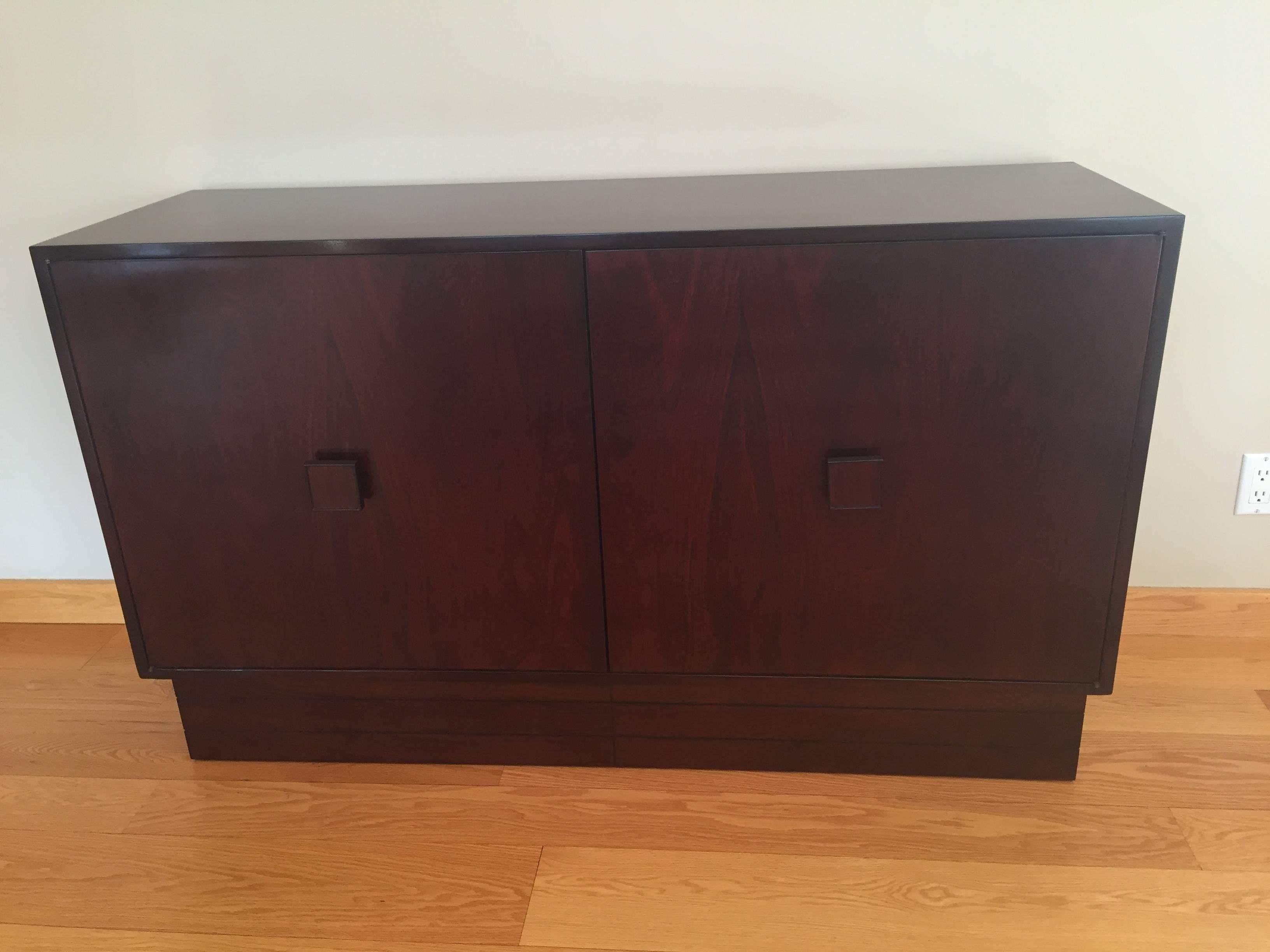 Mobile credenza a due ante in palissandro francese di piccole dimensioni, con interno a due ripiani e base a piedistallo. Design semplice con grande tiretto quadrato in palissandro.