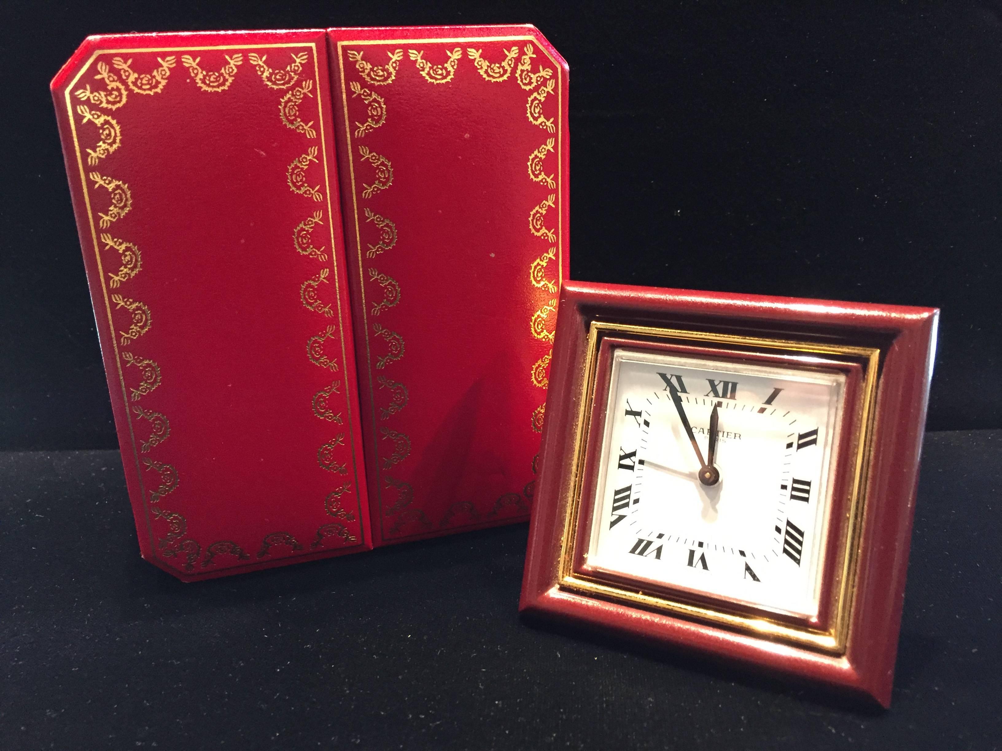 Le Must de Cartier burgundy red travel alarm clock, together with original Red gilt embossed travel box.

Travel size box exterior measurements 4.75