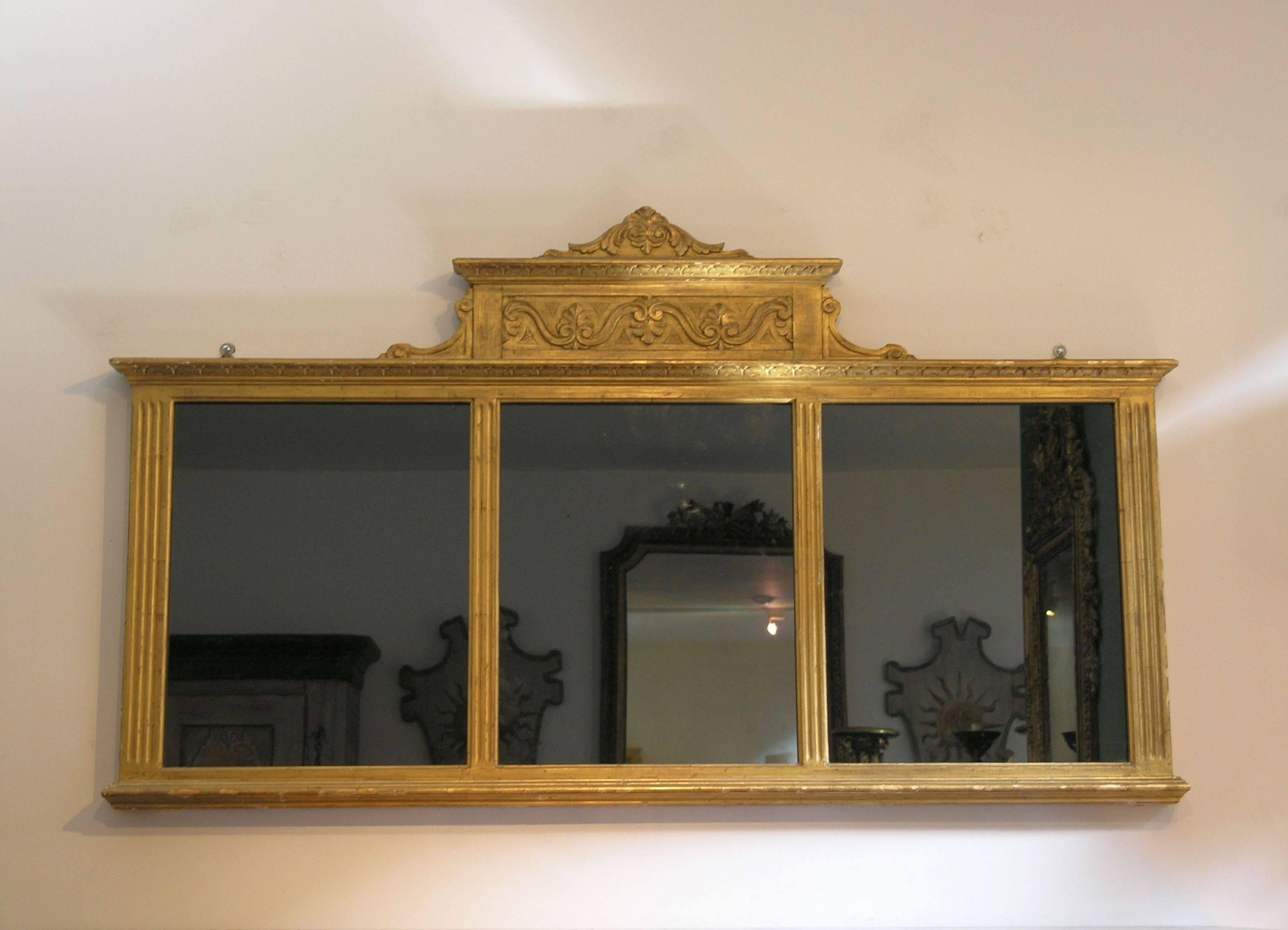 Horizontal giltwood three section wall mirror, the rectangular plates within molded divides, flanked by stiles ending on a plinth base.

 