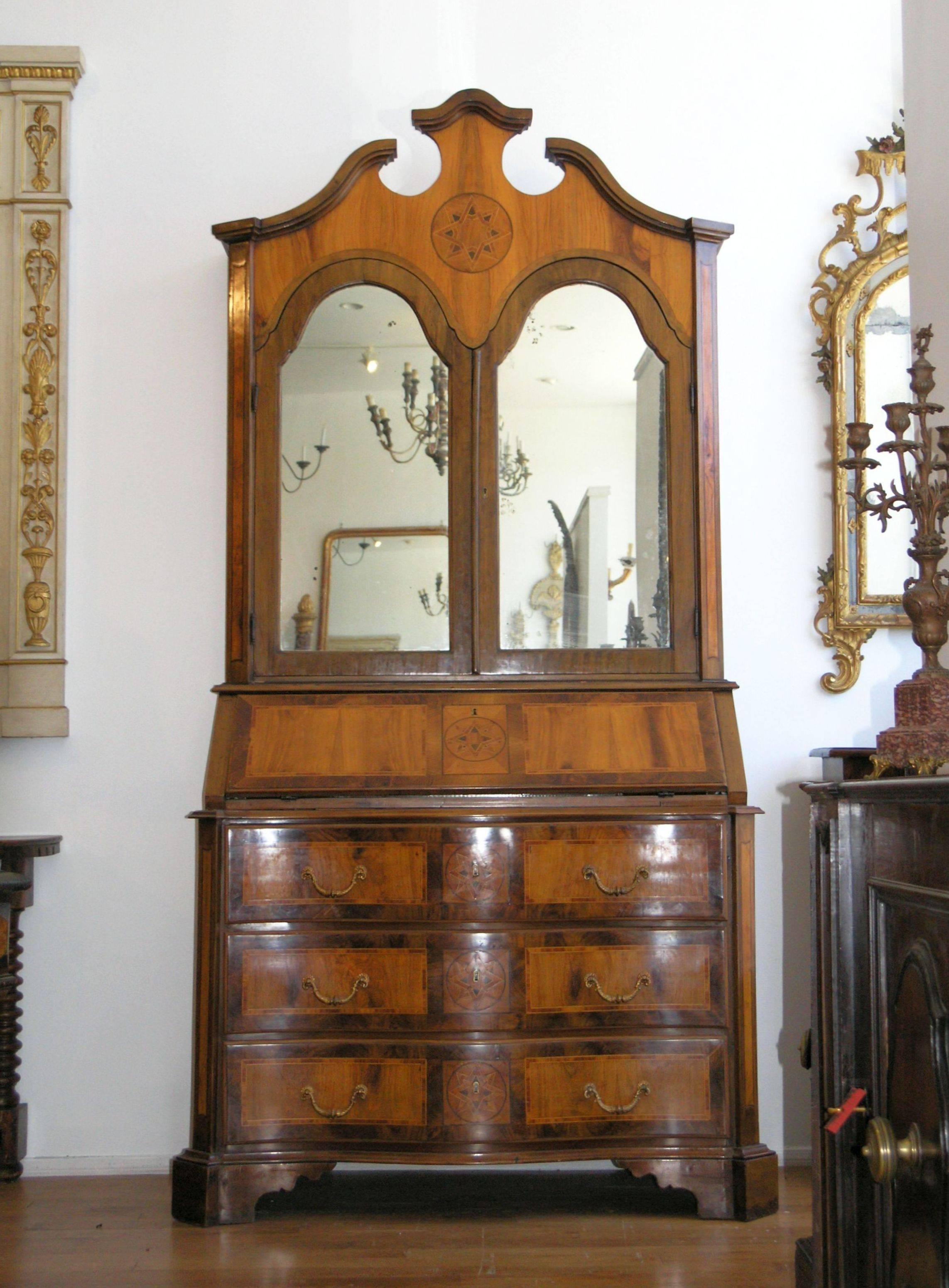 Southern Italian inlaid secretary. The upper case with swept broken pediment by a pair of arched mirrored doors, the lower case with hinged sloping fall enclosing a fitted interior above three long drawers of serpentine outline on bracket feet.