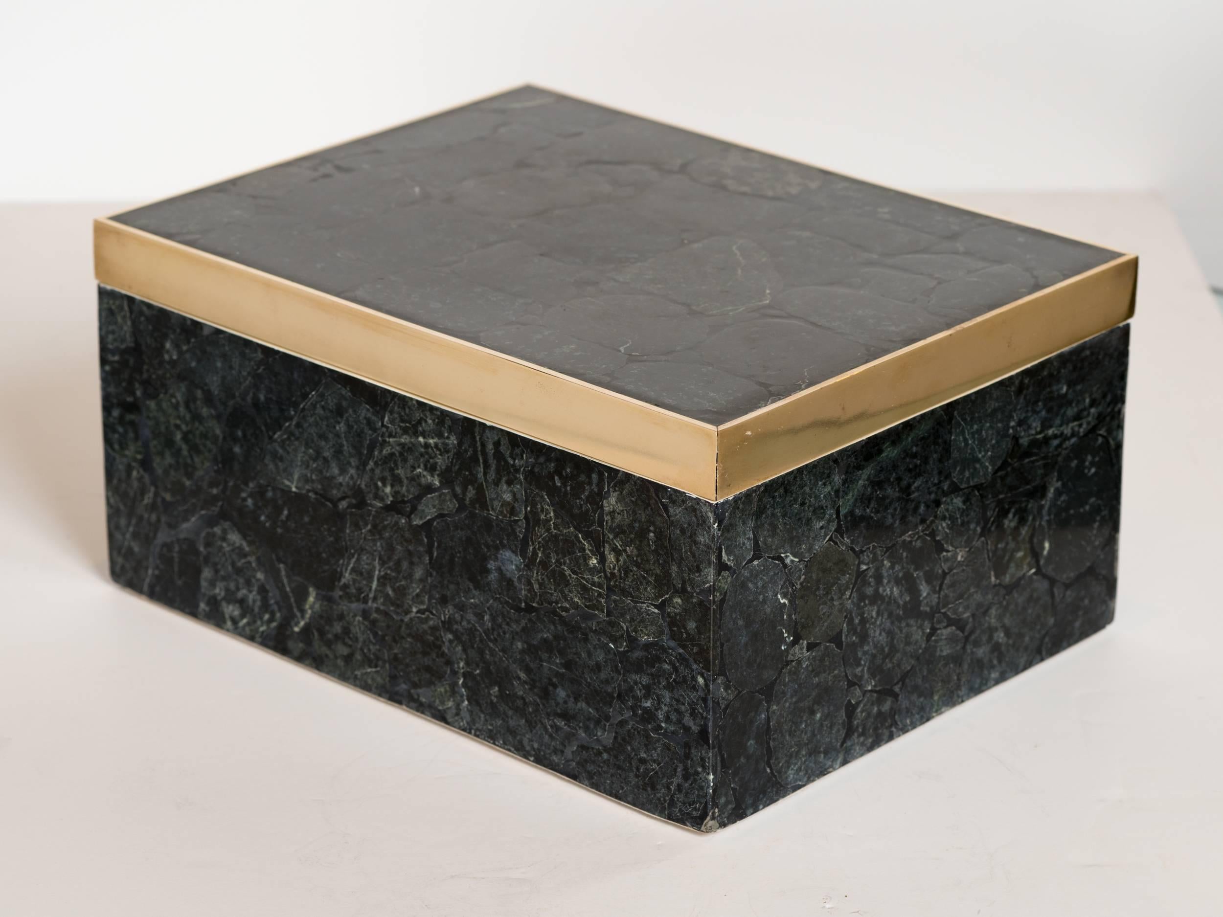 Handsome handcrafted decorative box comprised of black agate stone. Stones form a mosaic pattern and feature varying hues of black and grey, with white and slight green veining throughout. The lid has a beautiful brass banded detail and the interior