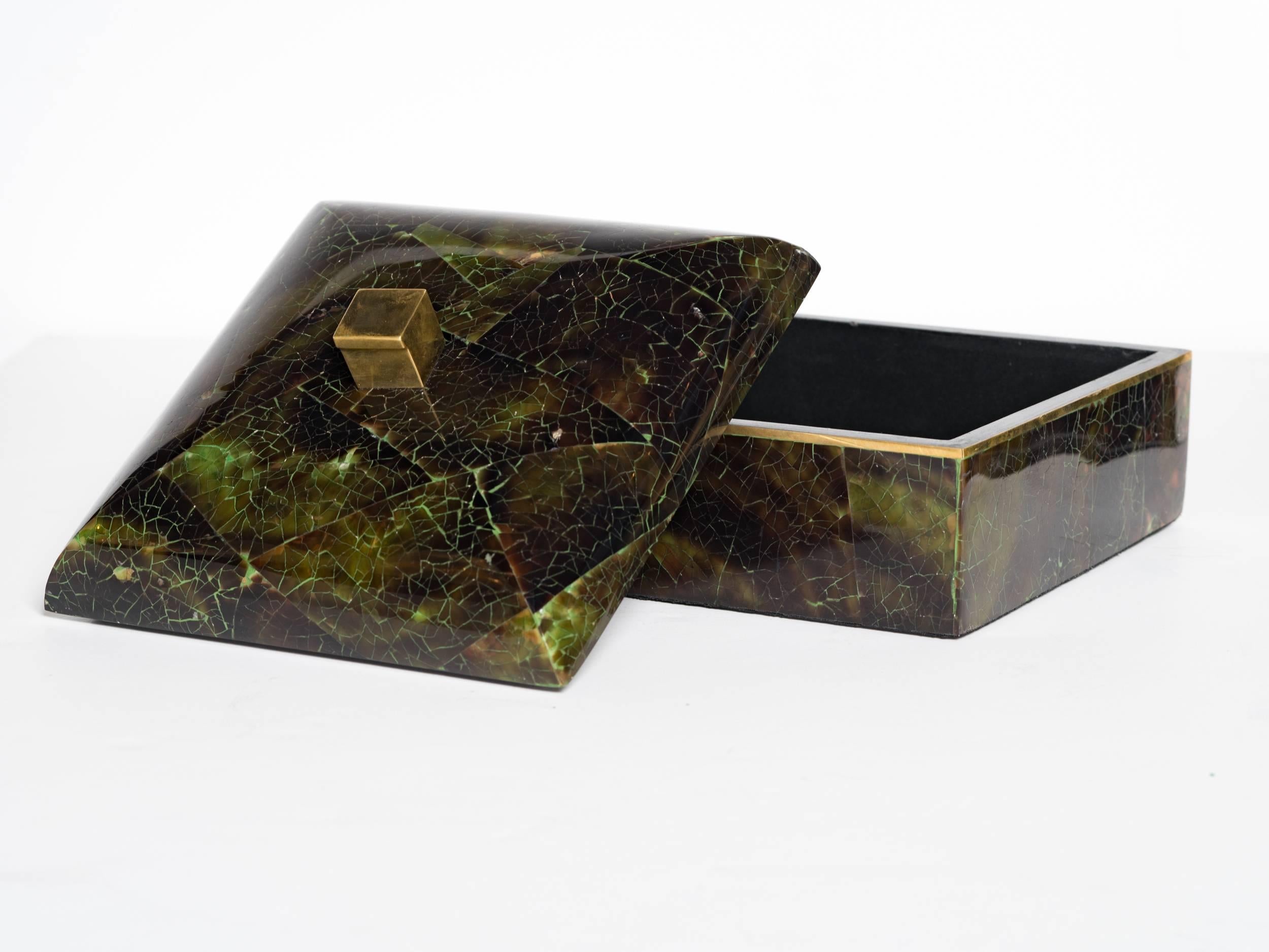 Exotic handcrafted decorative box comprised of lacquered natural green tab shell. The box has a chic square form with dome lid and features a stylized brass finial and brass trim detail. The box features a geometric pattern design and the interior