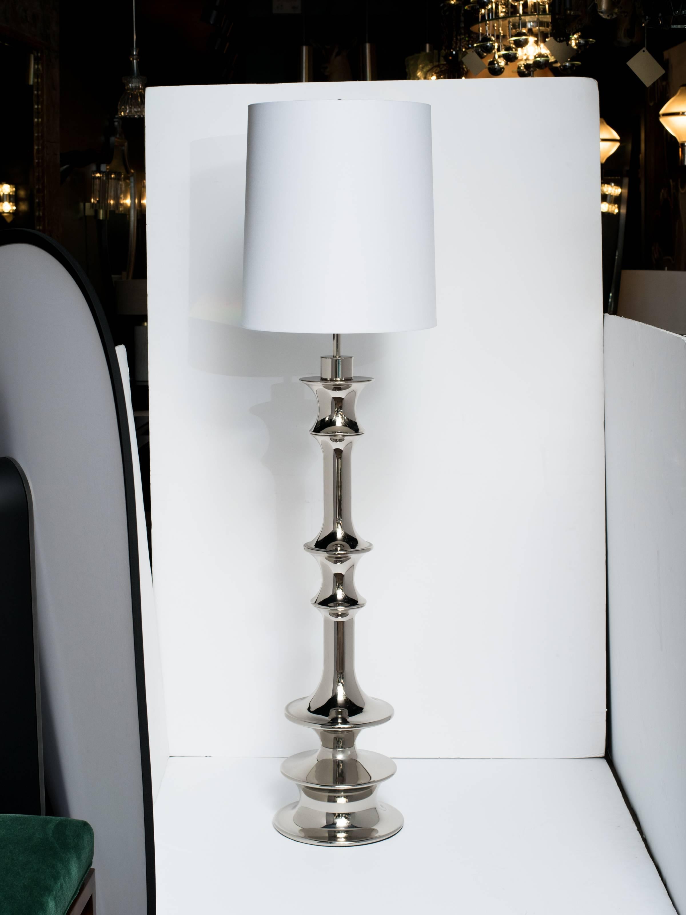 Pair of tall dramatic Hollywood Regency floor lamps with architectural design. Lamps feature highly stylized baluster forms in polished nickel finish. The sculptural design is reminiscent of Queen chess pieces.  Shown with drum shades in white.