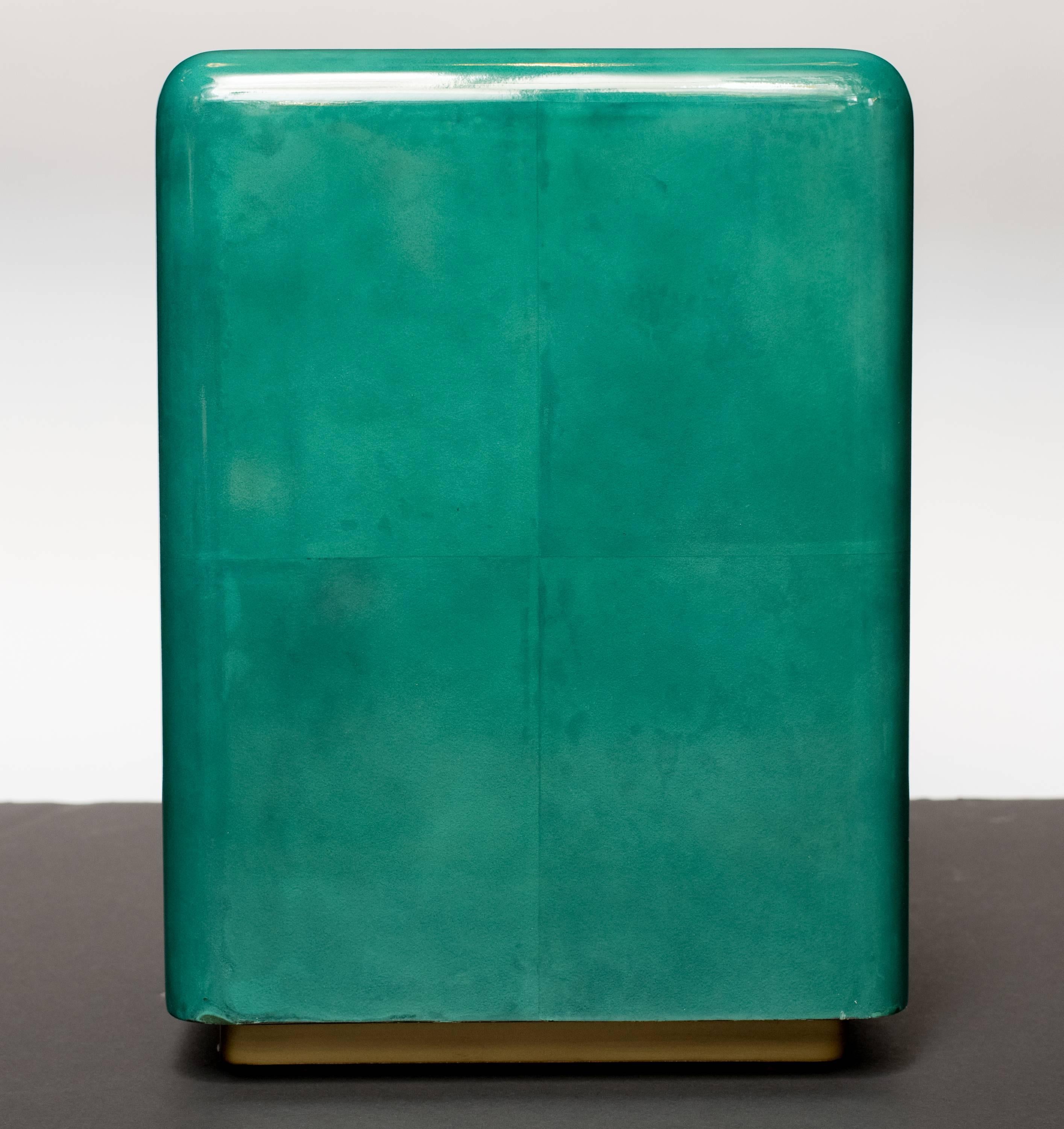 Outstanding handcrafted side tables with cube form and floating base design.
Comprised of lacquered goatskin or vellum over wood in hand-dyed hues of teal or turquoise. The tables feature streamline design with even parchment patchwork and a gold