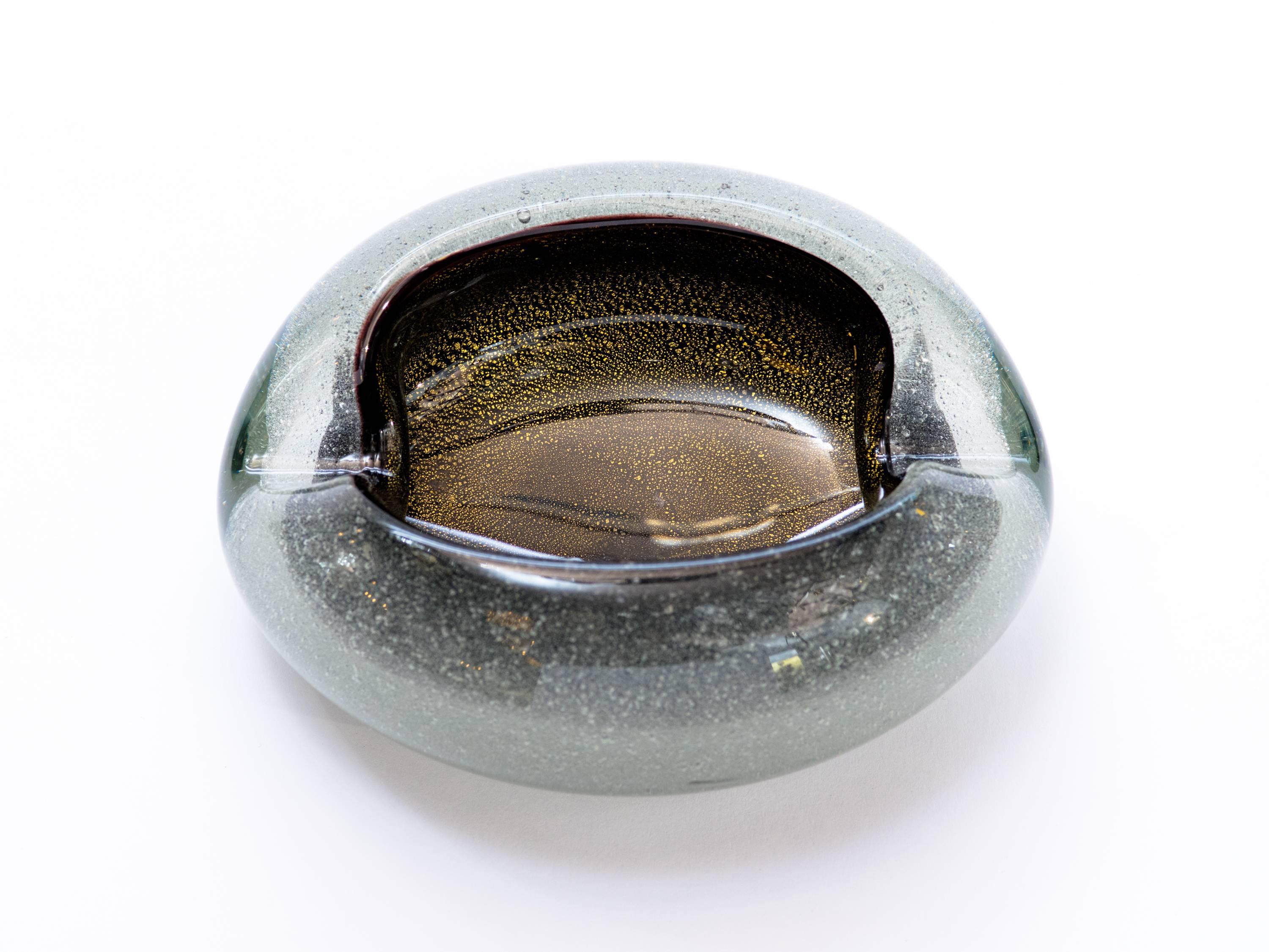 Stunning mid-century modern ashtray or bowl, comprised of handblown Murano glass. The ashtray has black glass interior with gold flecks details, and features gradient smokey grey exterior with iridescent speckles. The ashtray has an organic oval