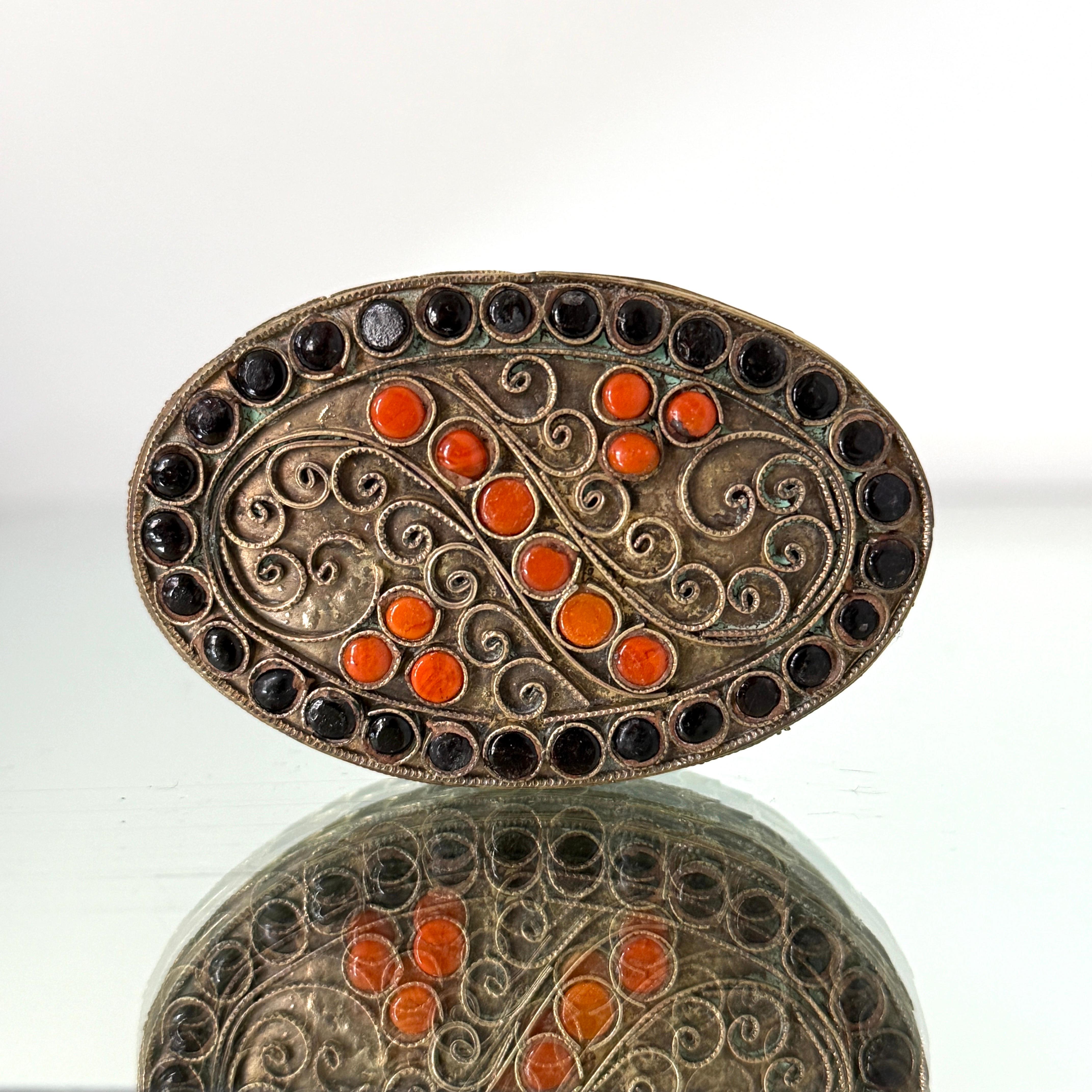 Boîte à bibelots en métal laitonné, fabriquée à la main, avec un motif filigrane. Il comporte des insertions de corail et d'onyx, des pierres semi-précieuses.  La boîte ovale est ornée d'une série de volutes gravées et d'un motif cachemire sur le
