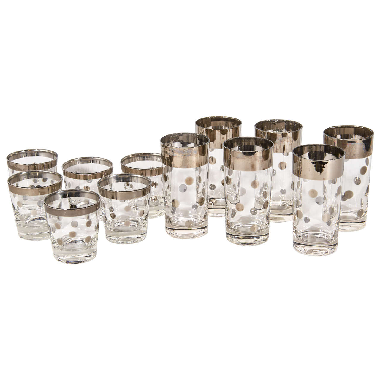 Set of 12 Mid-Century Modern cocktail glasses consisting of six highball glasses and six lowball or rock glasses. The glasses have a mercury silvered metal trim detail with polka dot design. Adds a smart and cheerful addition to any bar